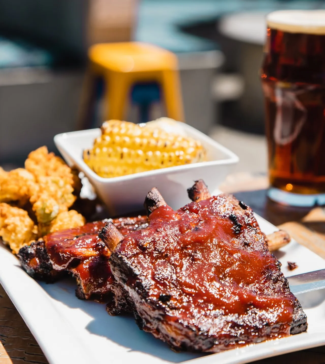 A delicious plate of barbecue ribs served with corn and fried food, alongside a beer.