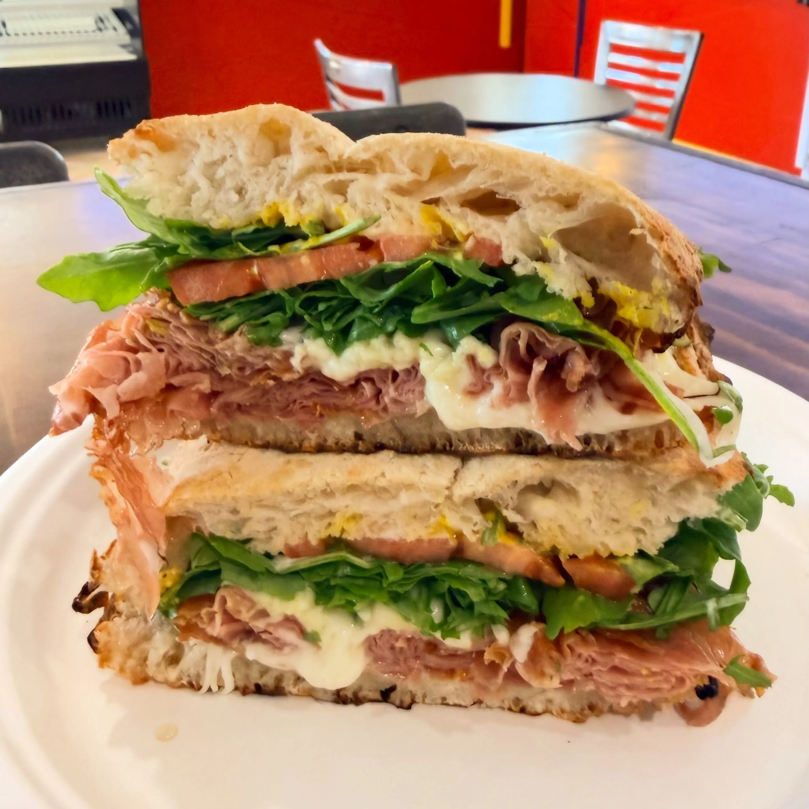 A large sandwich filled with layers of meats, greens, and condiments, presented on a white plate.