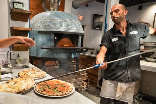 Pizzaiolo serving Margherita pizza from a wood-fired oven