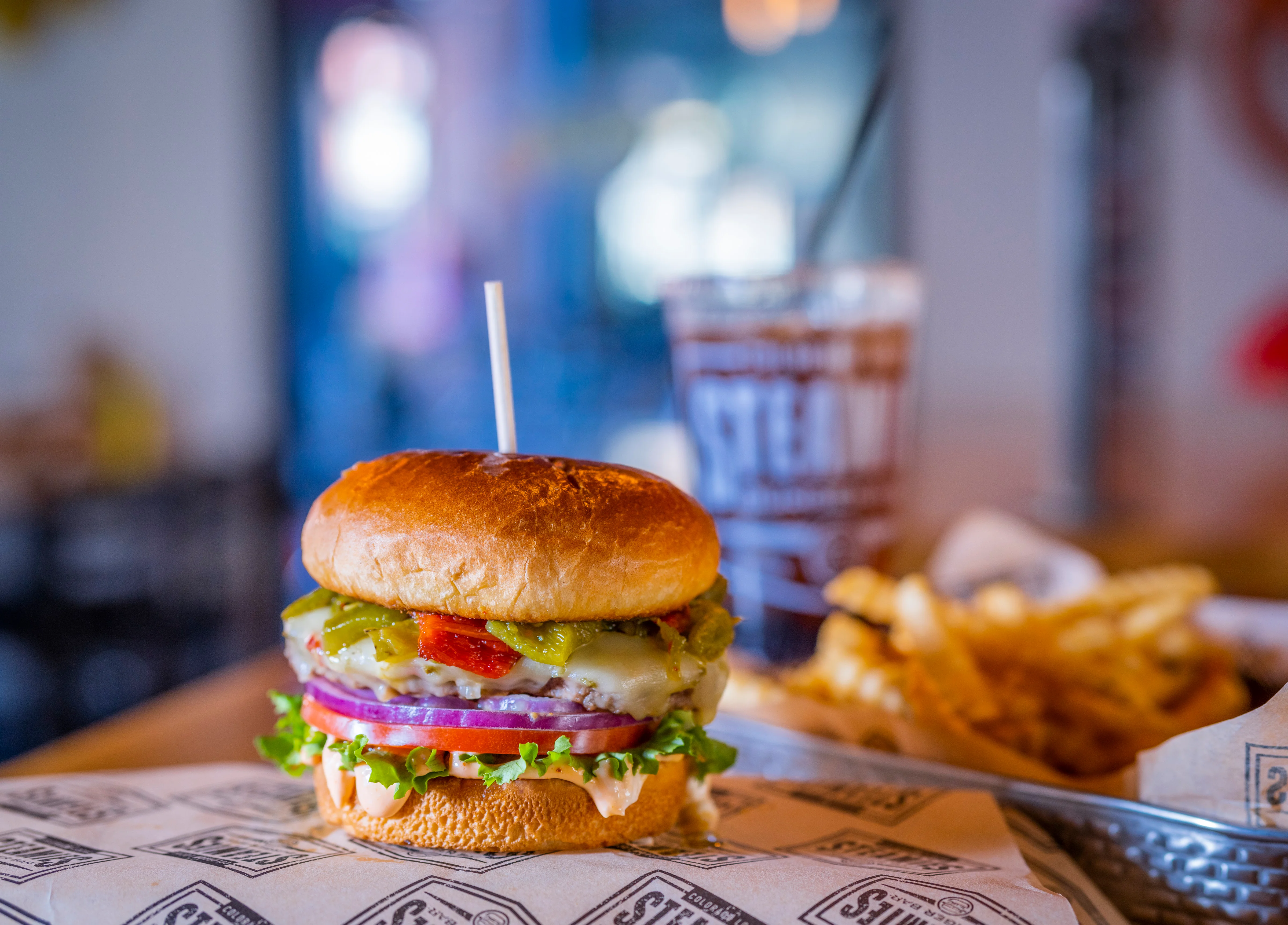 A classic hamburger with layers of pickles, onions, and lettuce, served on a soft bun with a side of fries and a drink.