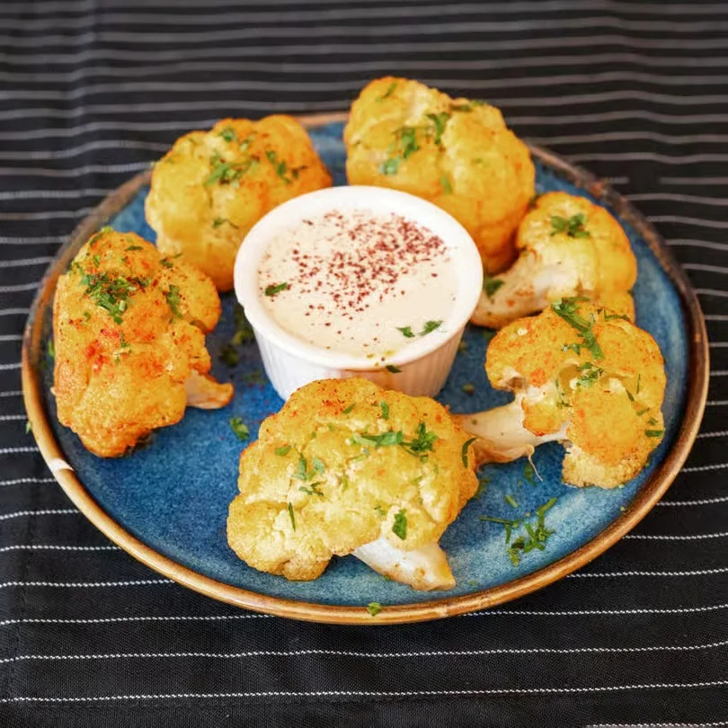 Fried cauliflower florets served with a creamy dip on a blue plate.