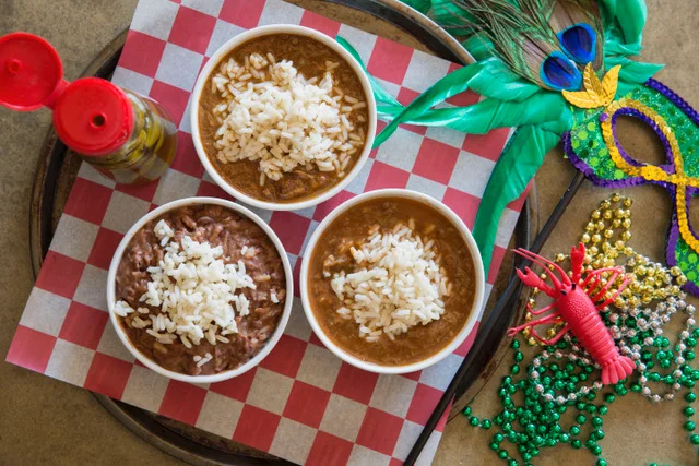 A bowl of hearty stew topped with rice, alongside cornbread muffins and a loaf of bread on a wooden platter.