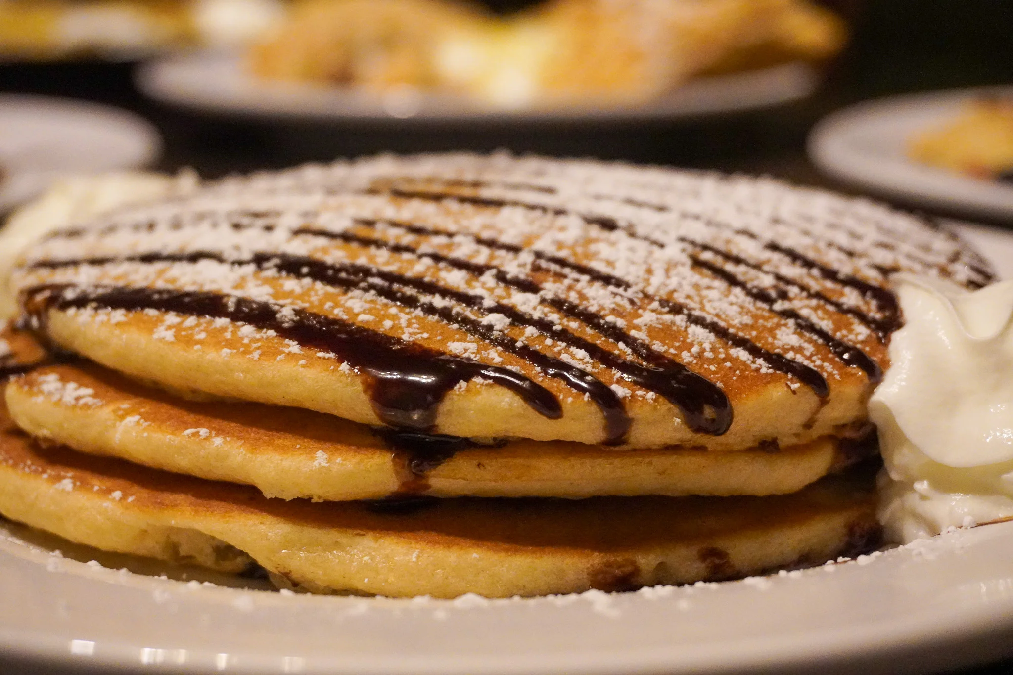 Fluffy American pancakes drizzled with chocolate sauce and powdered sugar