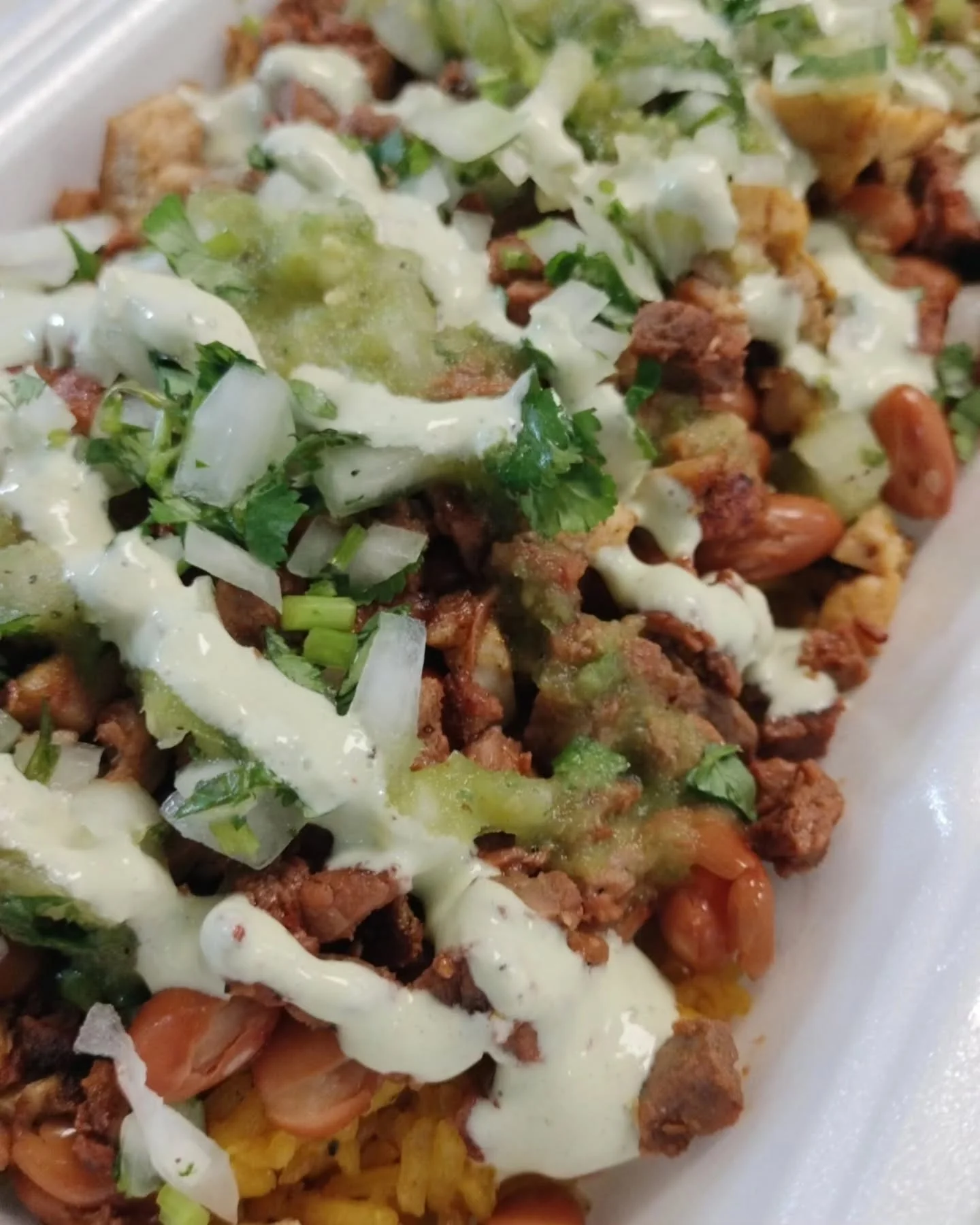 A hand holding a taco filled with grilled meat and melted cheese, with additional tortillas visible underneath. The presentation is vibrant and appealing.