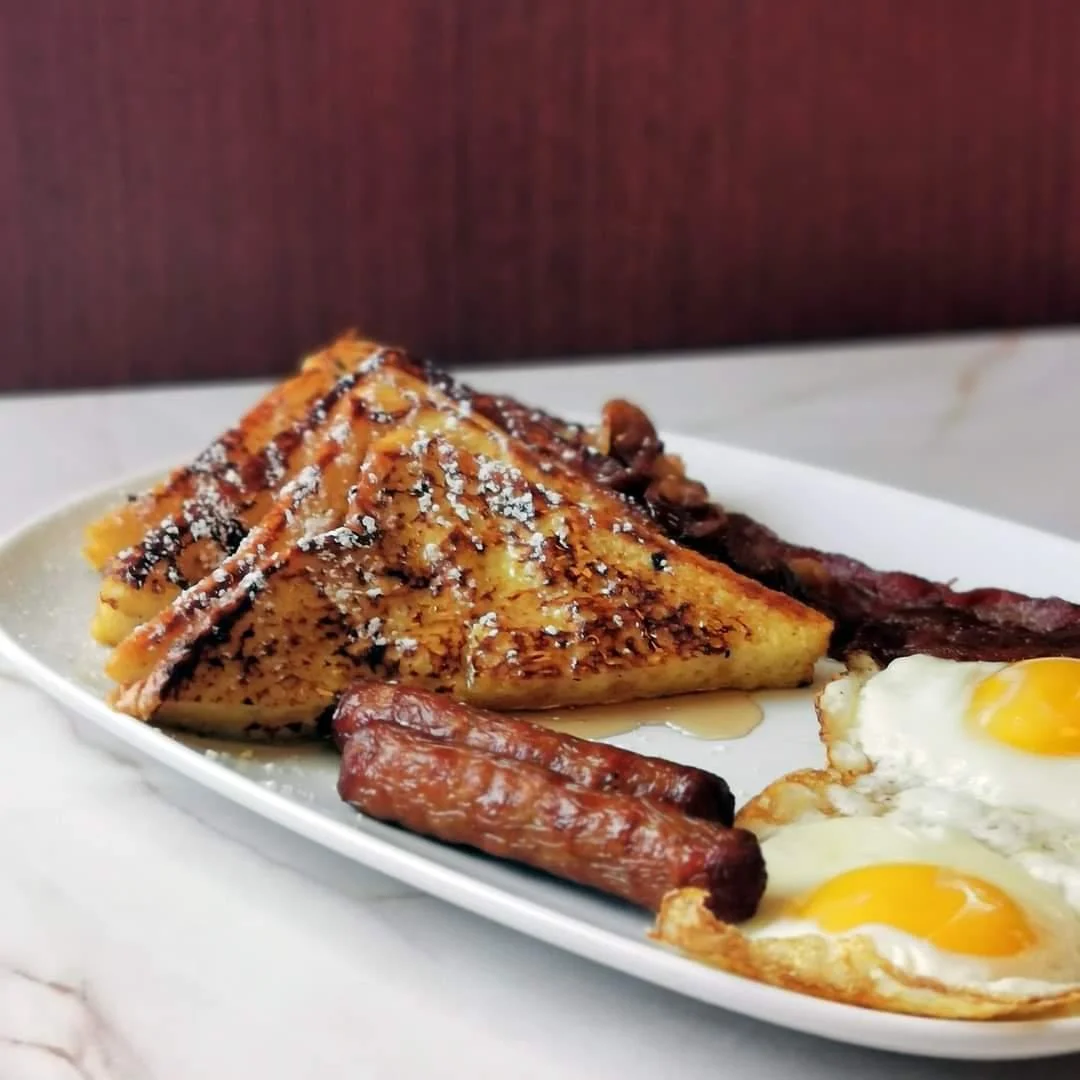 Moonlite Diner breakfast plate with golden French toast, sunny-side-up eggs, crispy bacon, sausage links, and maple syrup.