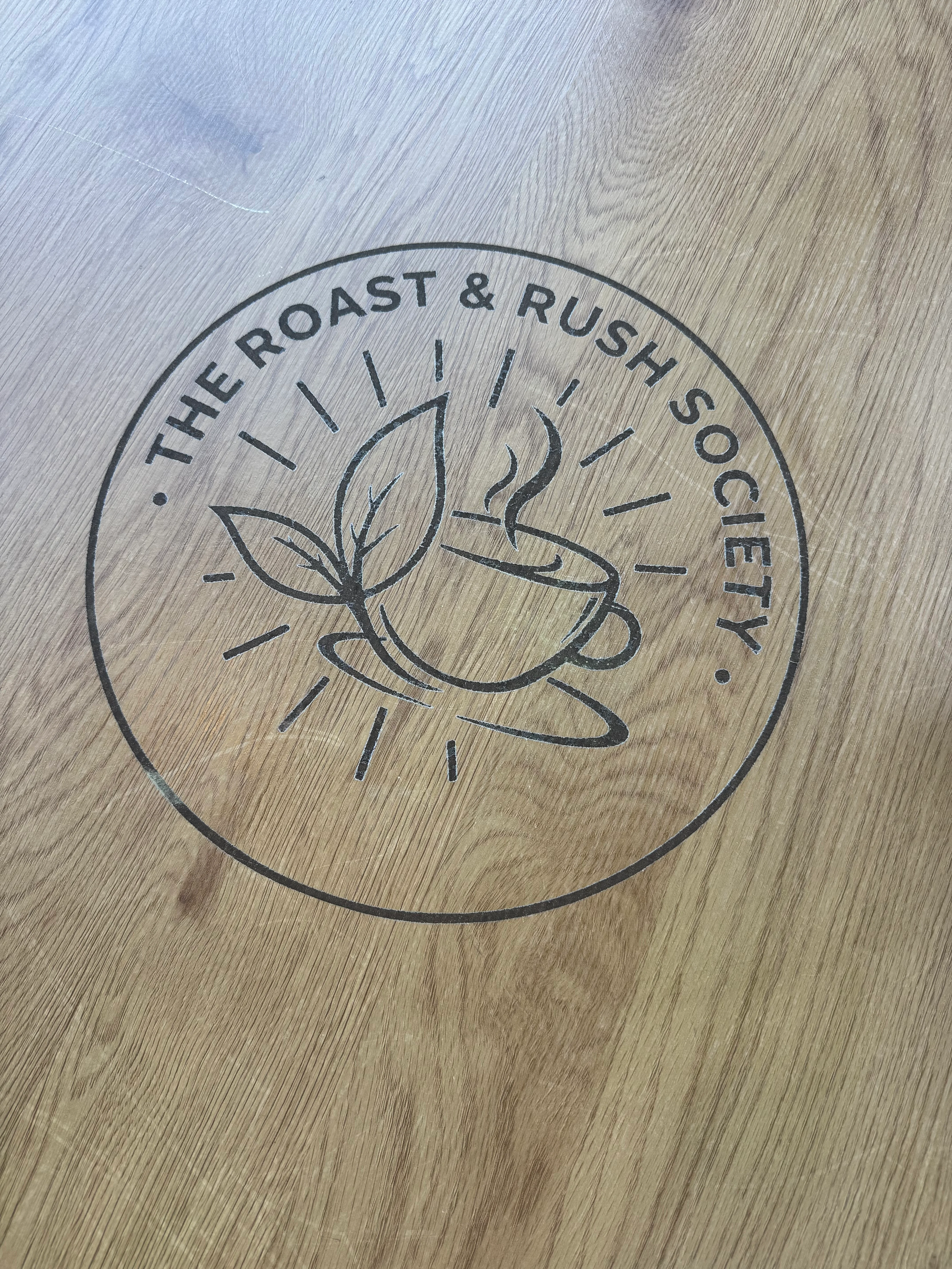 Logo of The Roast & Rush Society on a wooden table surface.