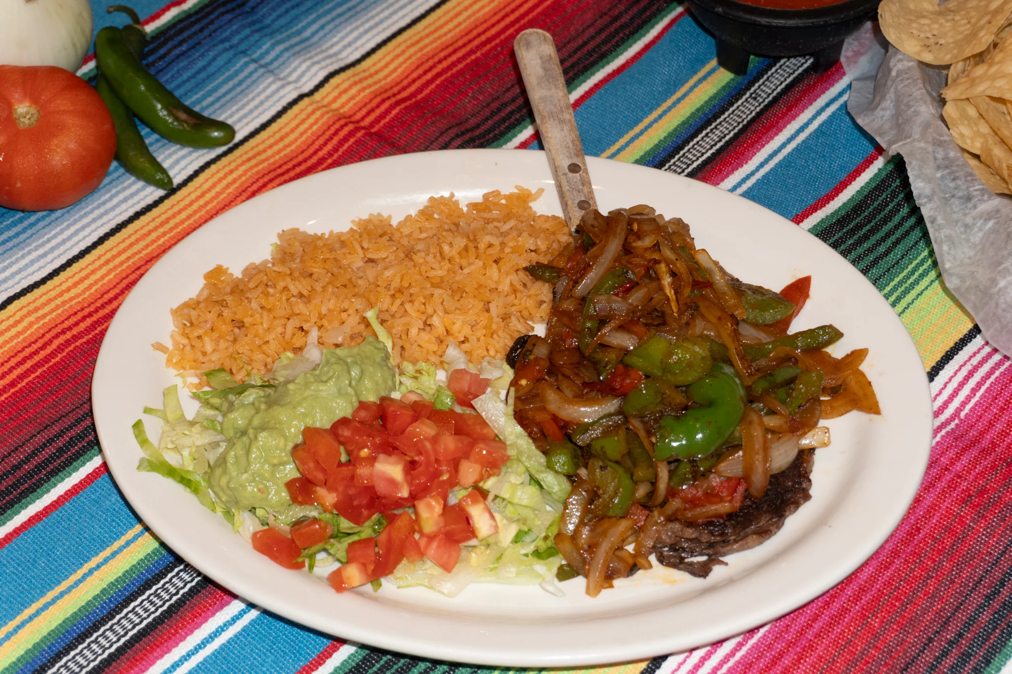 Sizzling fajitas served with rice, guacamole, and fresh vegetables on a vibrant tablecloth