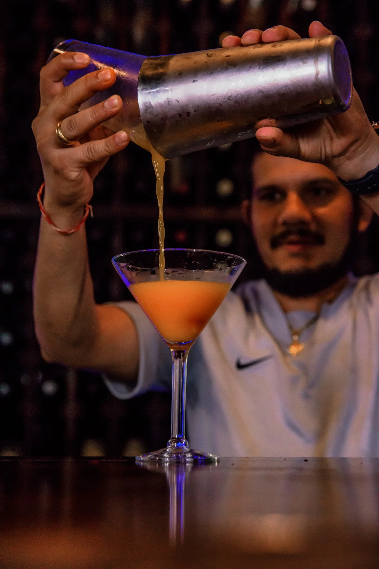 A bartender at Mint Indian Restaurant and Lounge expertly pouring a freshly shaken, handcrafted cocktail into a martini glass.