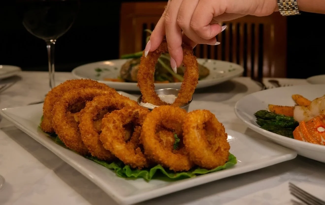 A platter of crispy onion rings served on a bed of lettuce with a small bowl of dipping sauce.