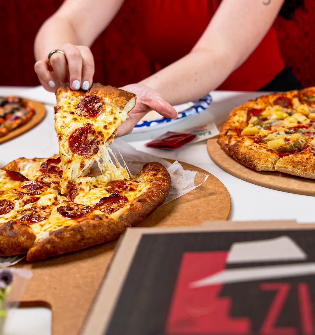 A hand reaching for a slice of pepperoni pizza with melted cheese.