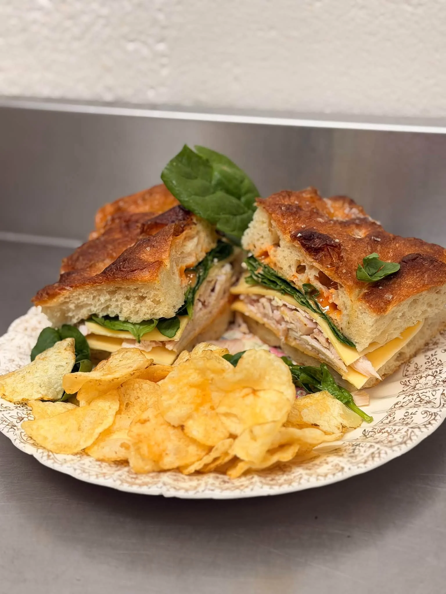 Gourmet sandwich with layers of meat and cheese served with potato chips