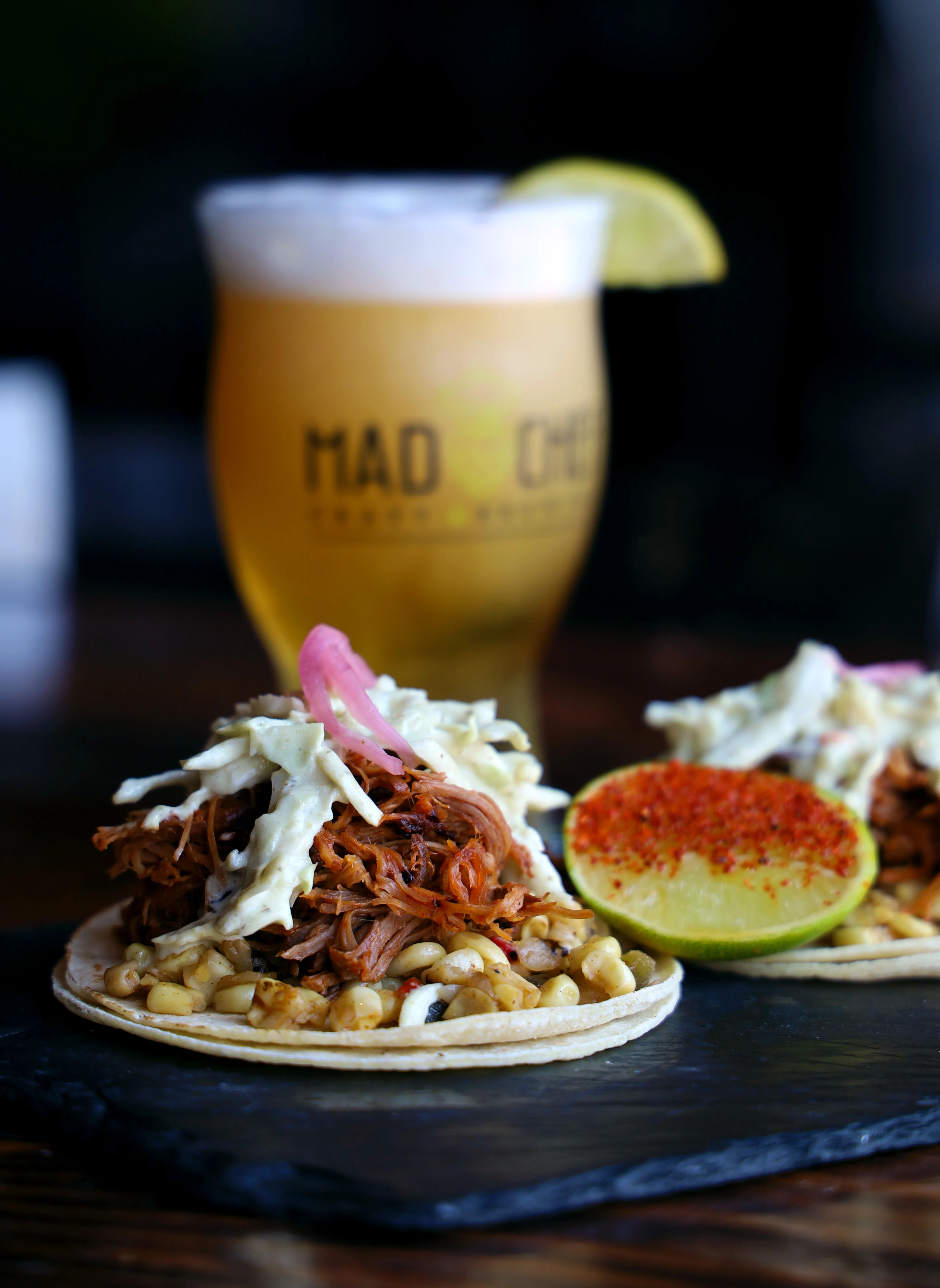 Three tacos with pulled meat, pineapple, and lime on a plate.