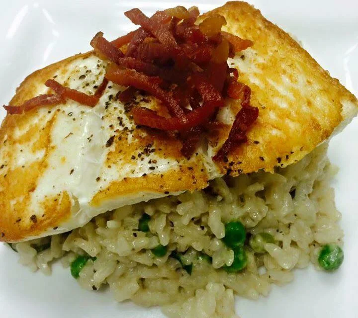 A beautifully plated dish of seared fish on a bed of creamy risotto, garnished with crispy bacon bits.