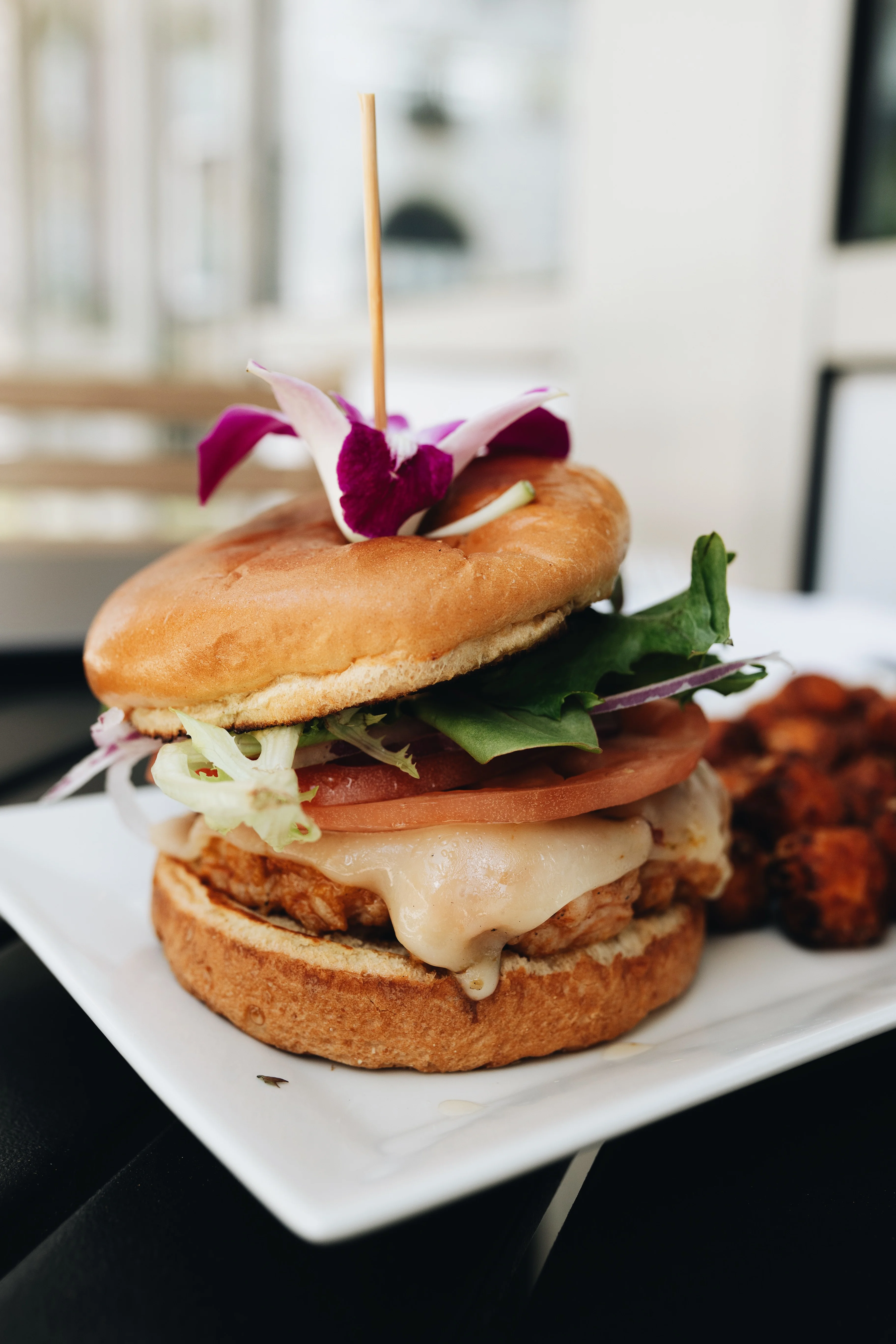 Crispy chicken sandwich with fresh toppings and edible flower garnish