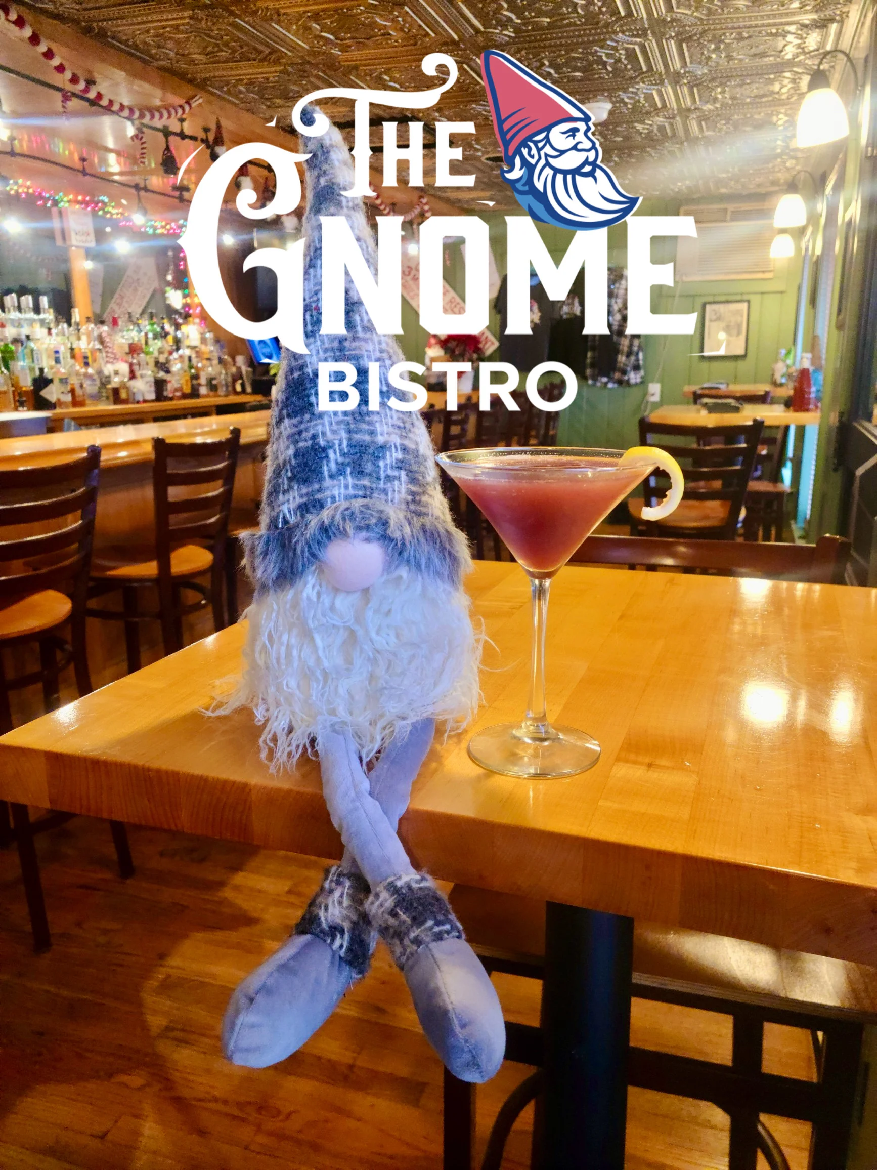 An indoor dining scene showcasing a plush gnome doll and a cocktail on a wooden table, with a warm and welcoming bar in the background.