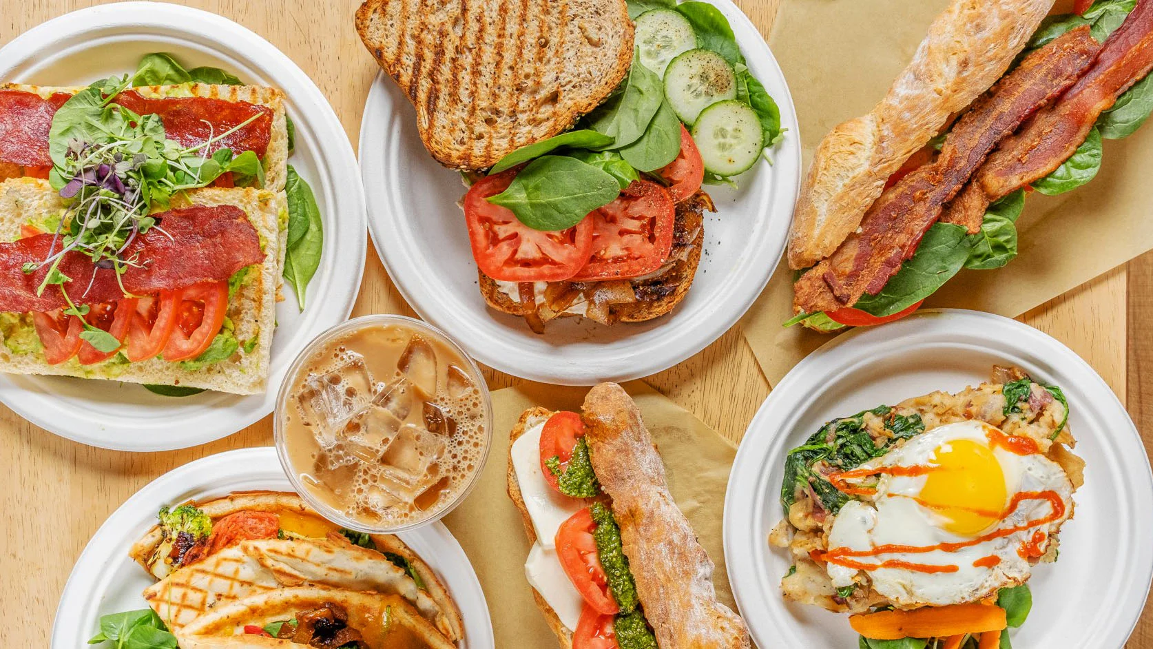 Assorted gourmet sandwiches and iced coffee on a wooden table