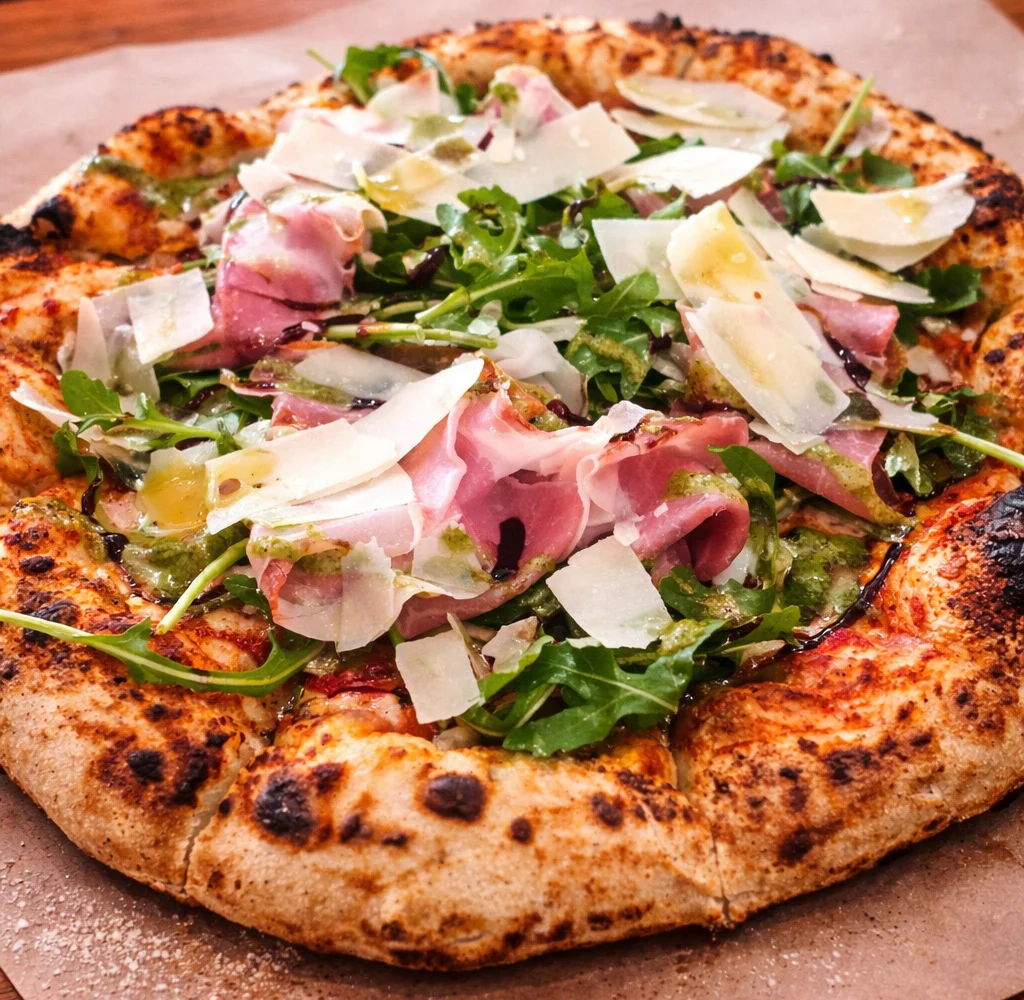 Italian prosciutto pizza topped with arugula and parmesan