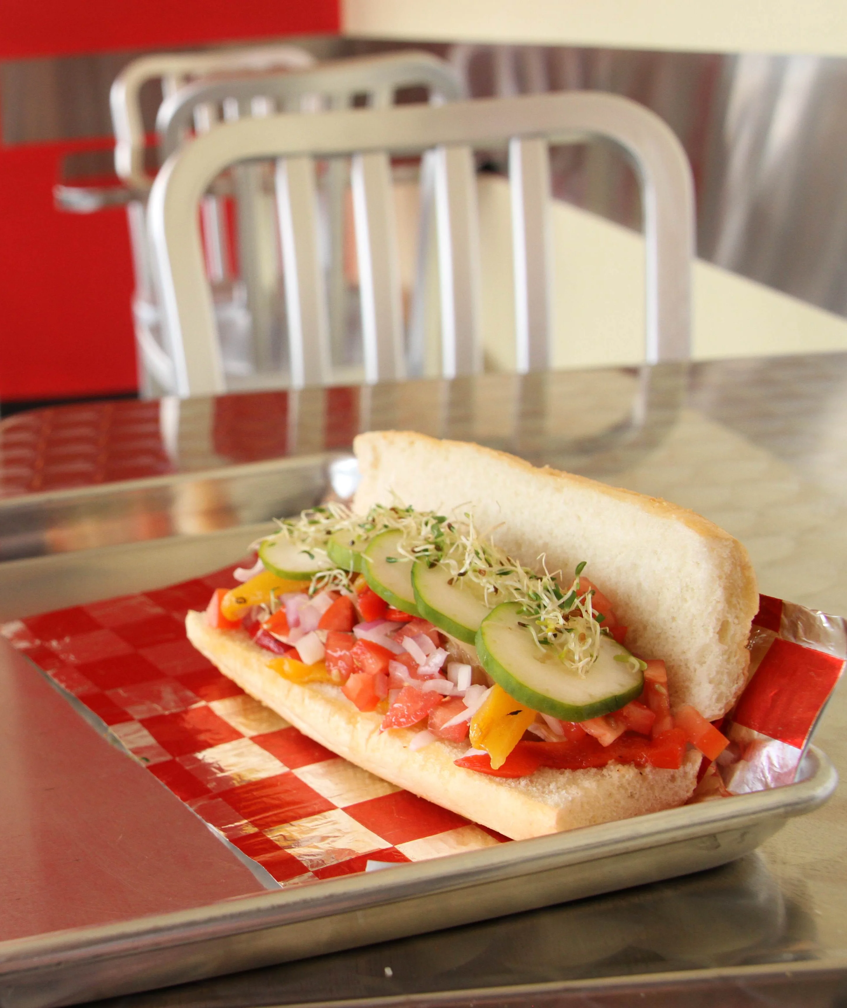 Fresh veggie sub sandwich with diced tomatoes, onions, bell peppers, cucumber slices, and sprouts on a soft hoagie roll, served on a metal tray at TJ’s Sandwich Shop in Northwest Arkansas