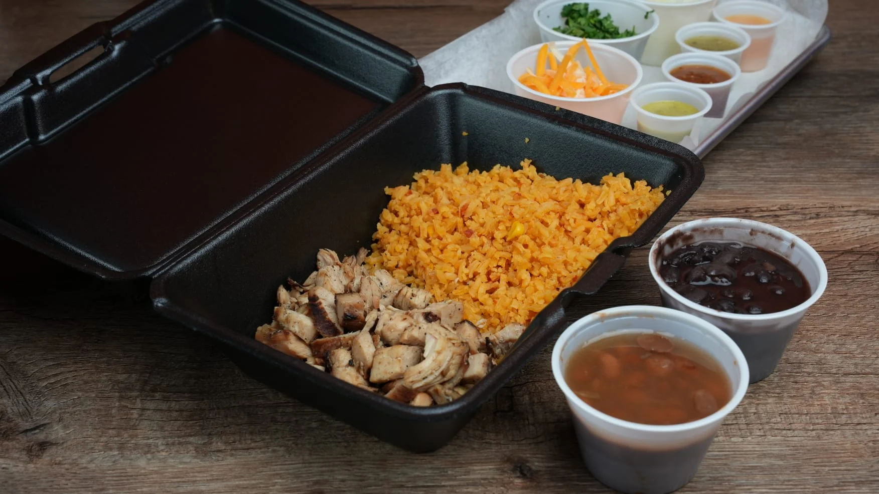 Grilled chicken with Mexican rice and beans in a takeout container