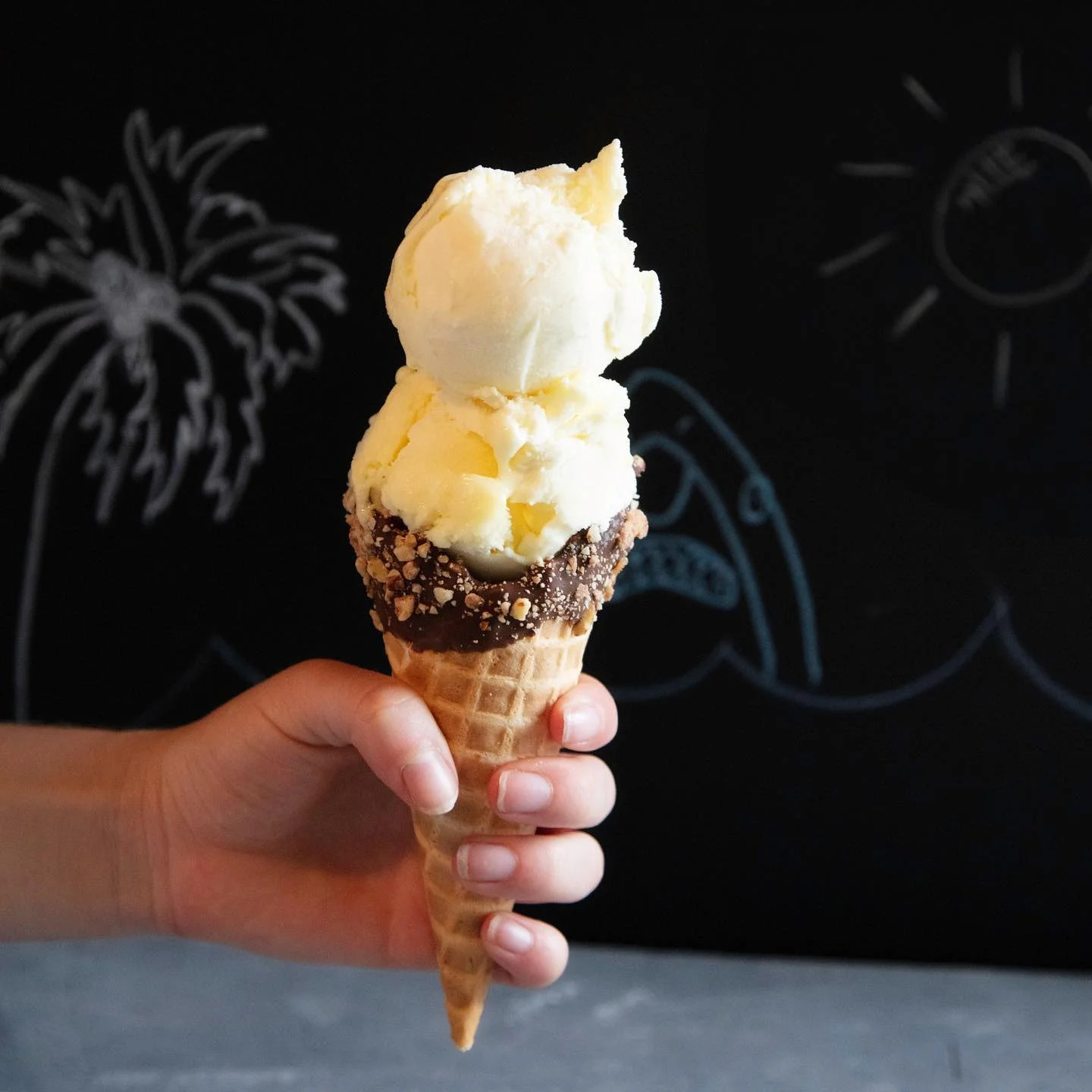 Hand holding a double scoop ice cream cone with chocolate and nuts.