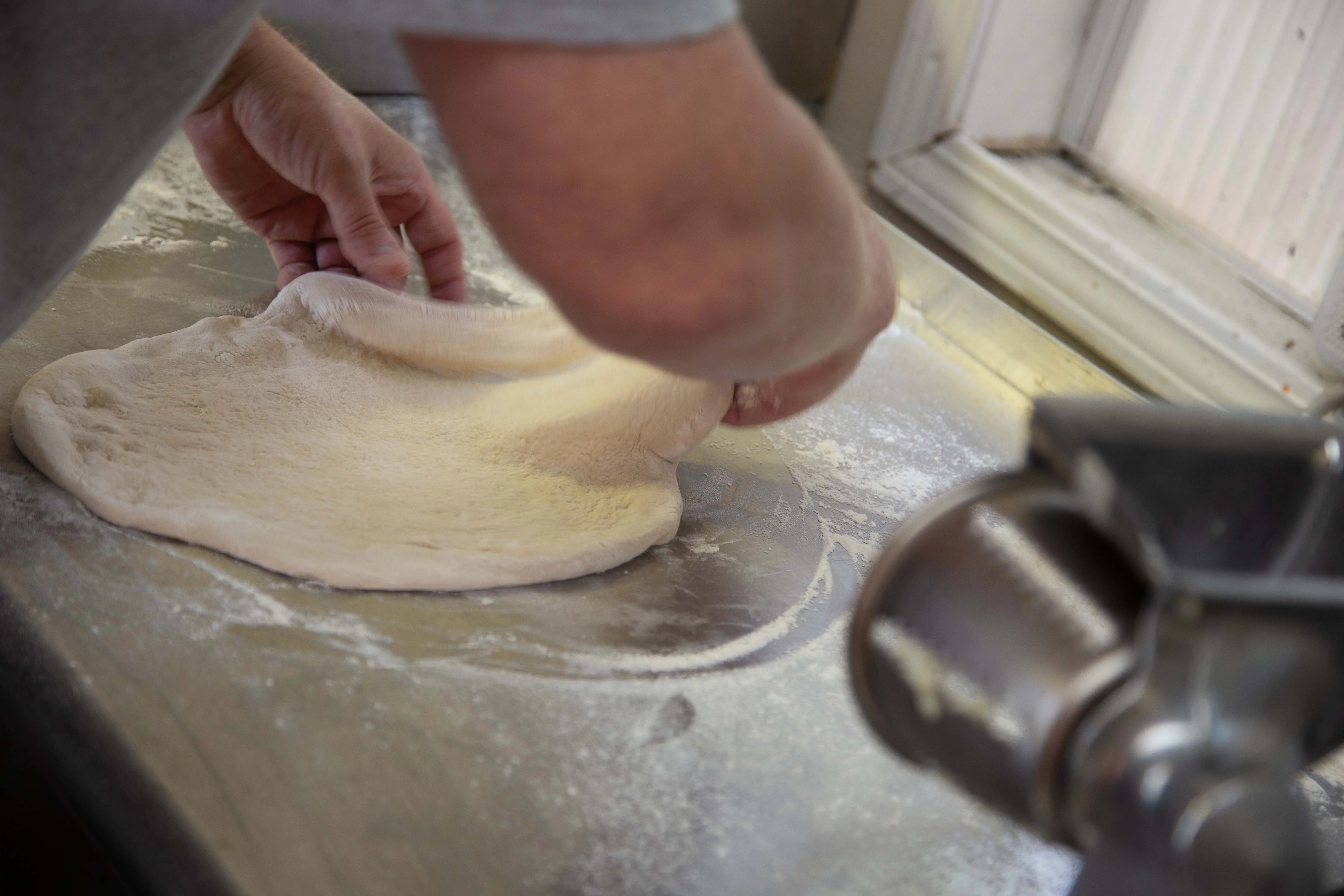 Chef stretching pizza dough on a floured surface