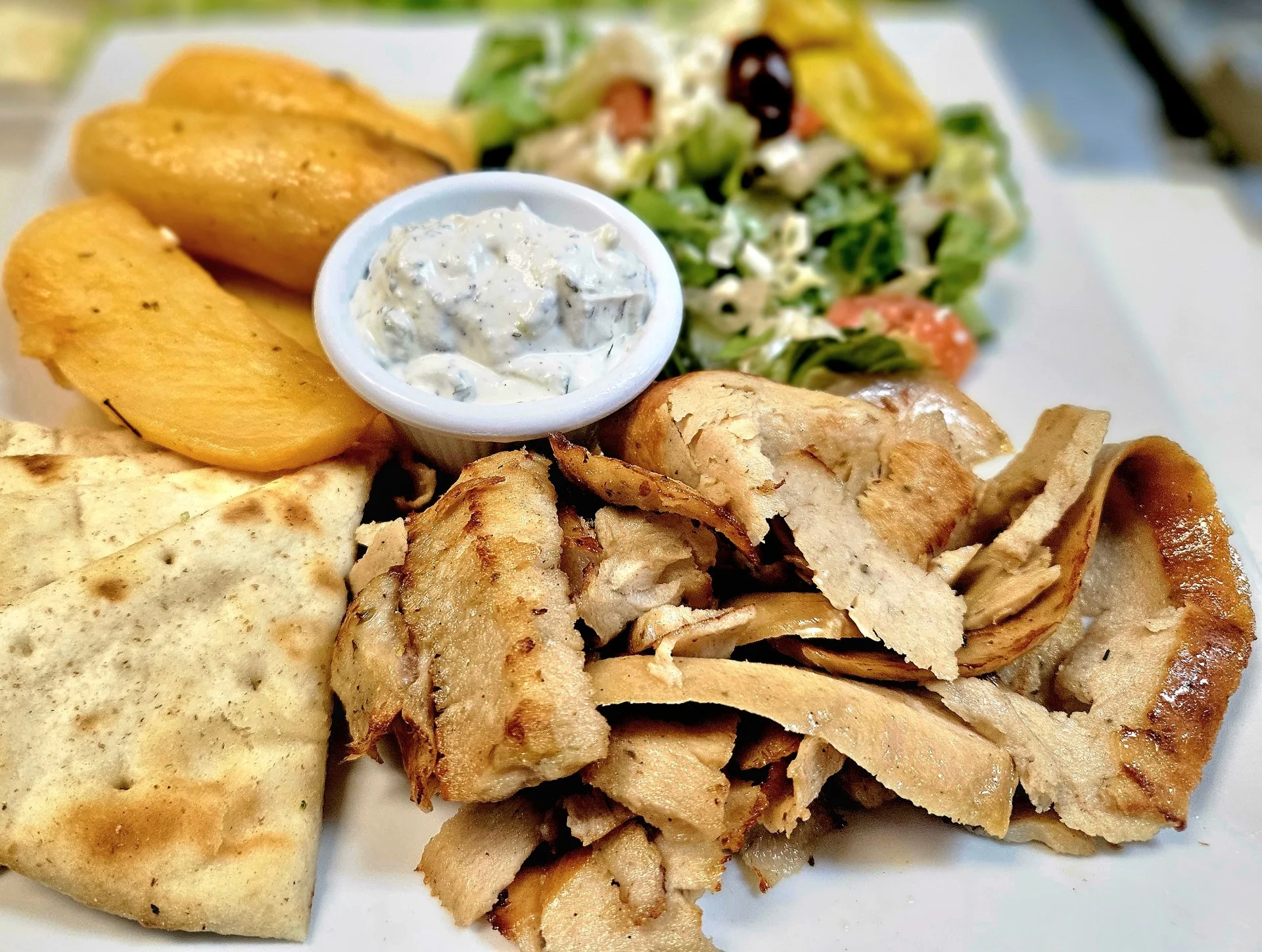 Greek chicken gyro platter with pita, potatoes, salad, and tzatziki
