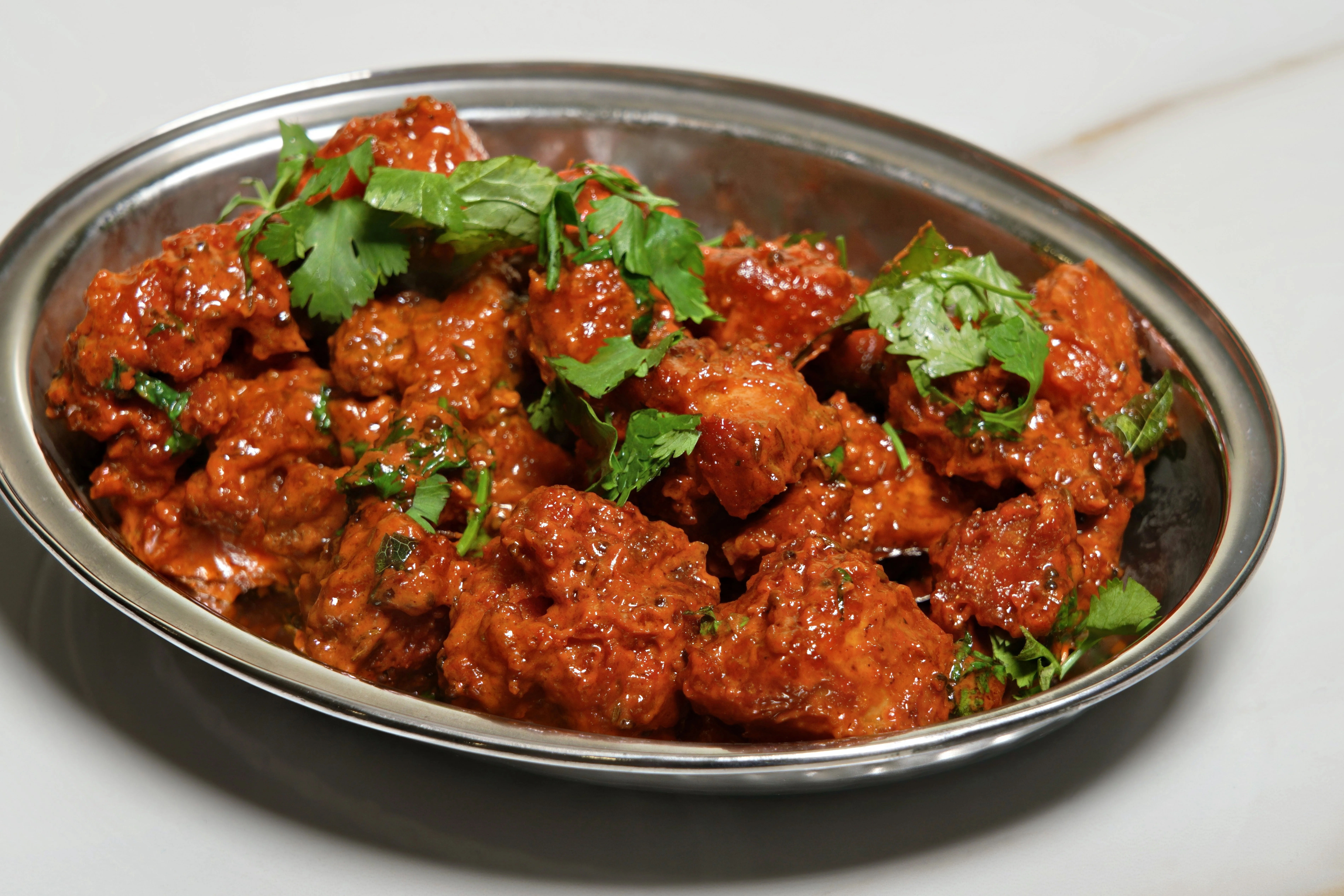 A plate of spicy chicken pieces garnished with fresh cilantro in a rich red sauce.