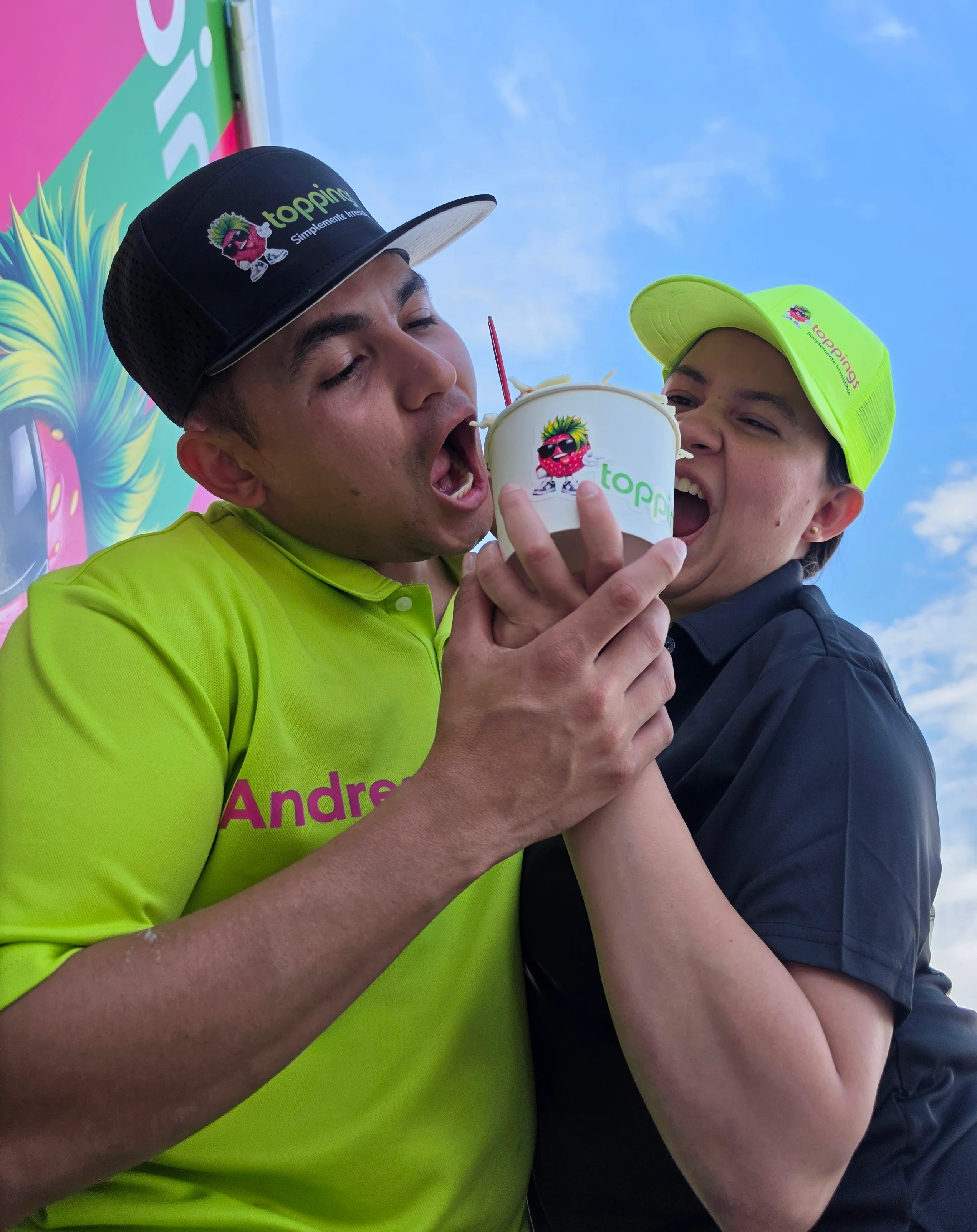 Two employees playfully sharing a dessert outside a colorful restaurant.