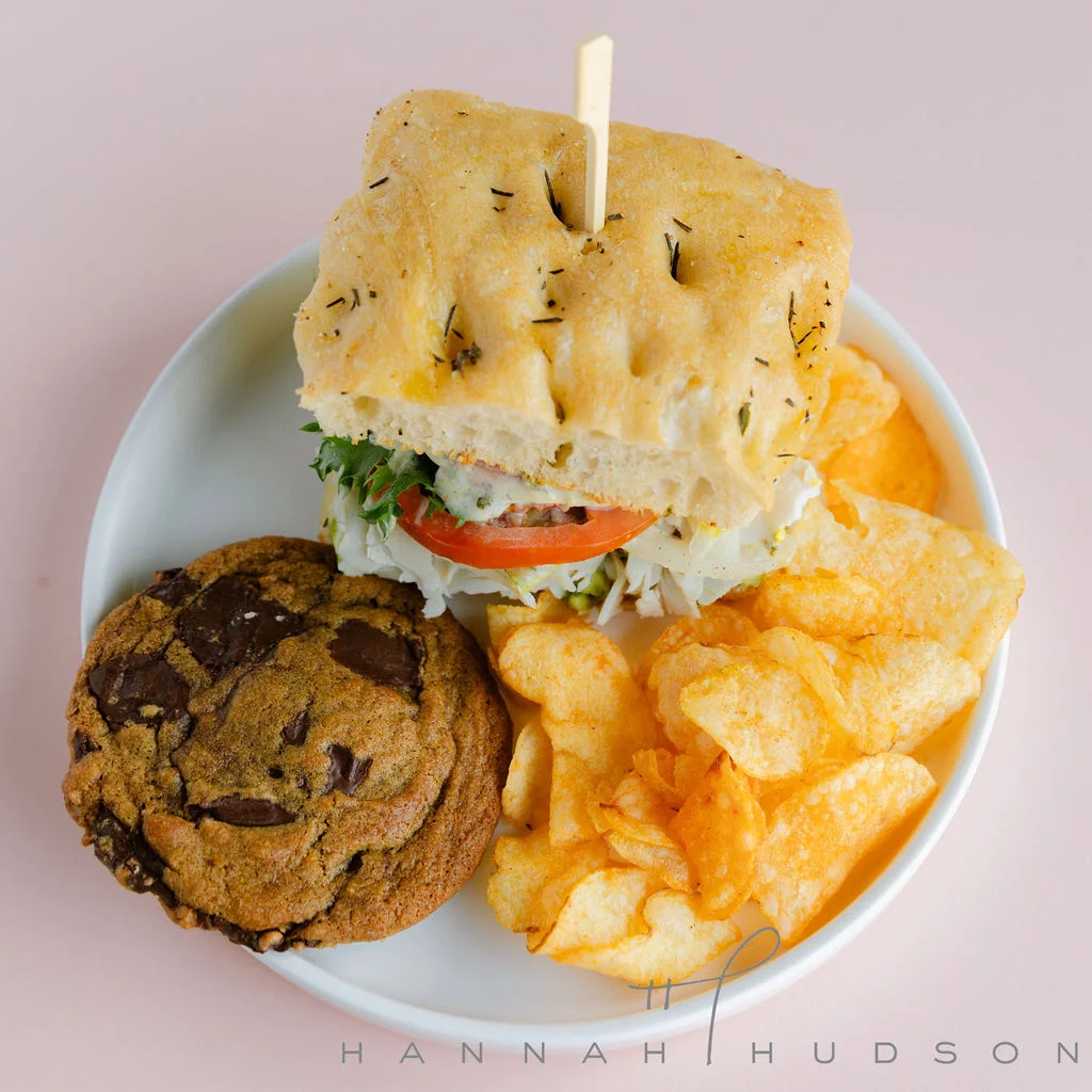 Focaccia sandwich served with potato chips and a chocolate chip cookie