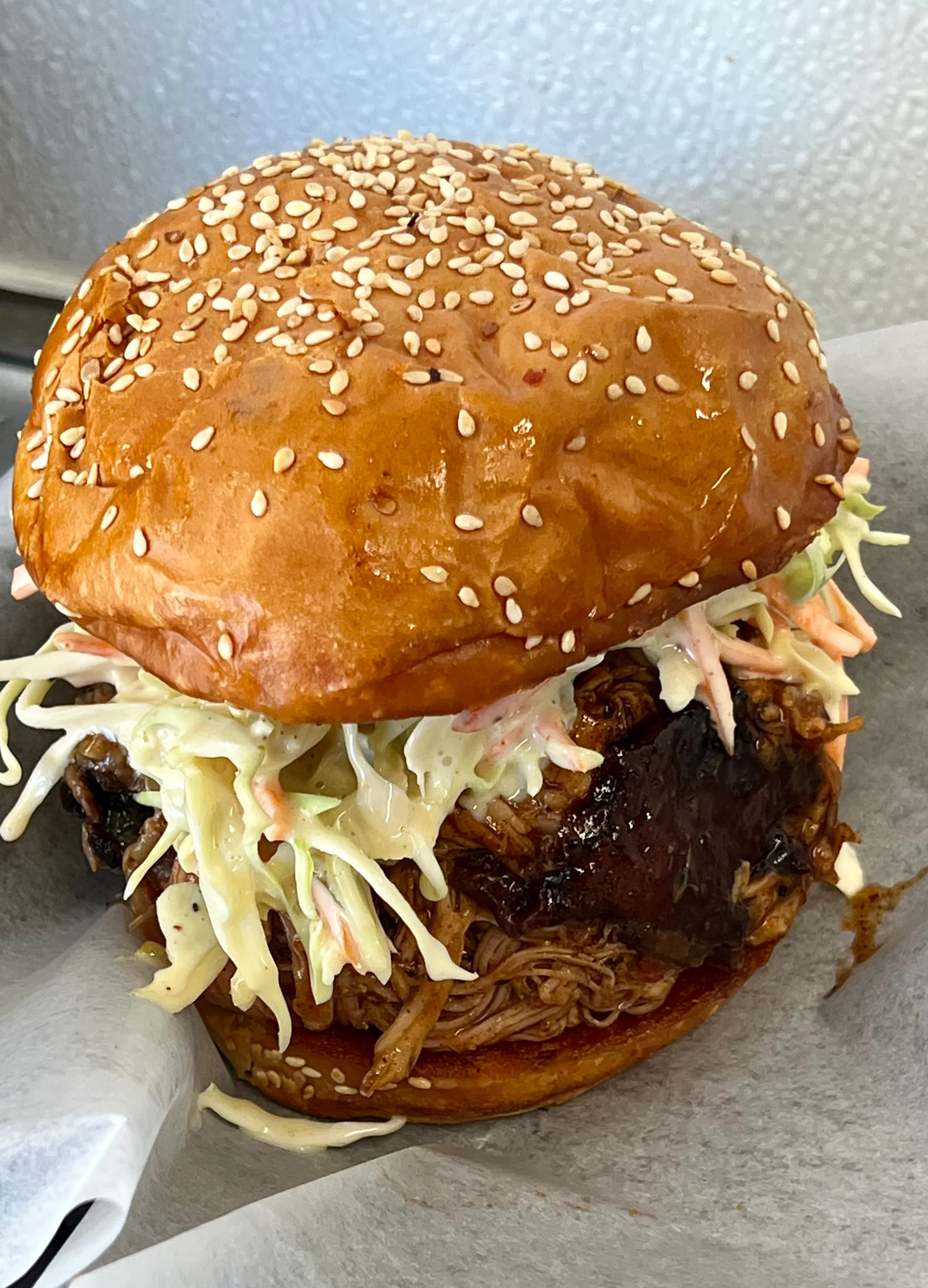 A delicious pulled pork burger topped with coleslaw, nestled in a sesame seed bun.