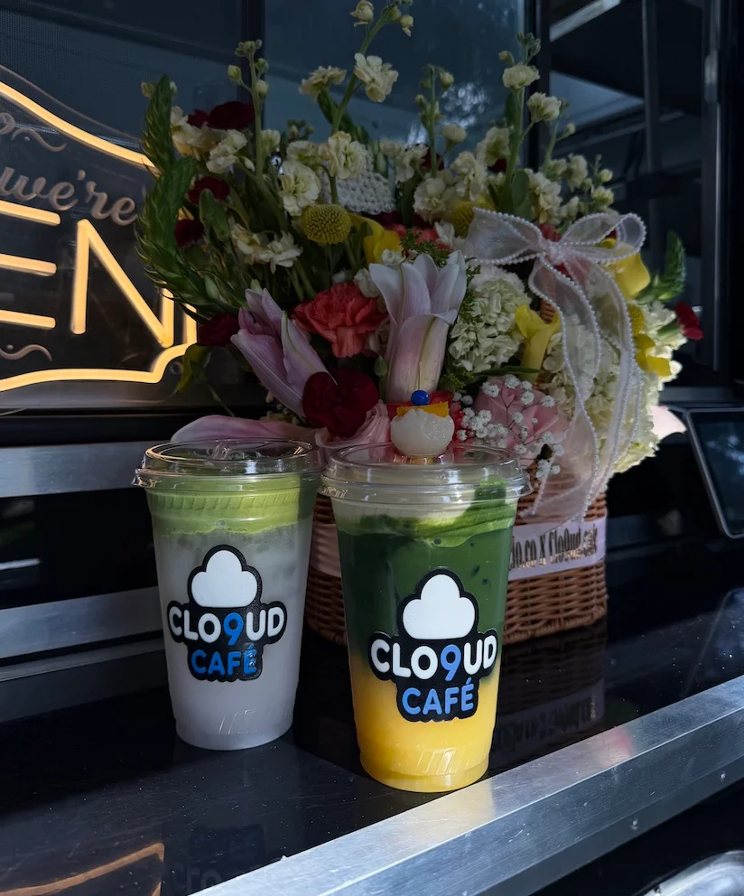 Two colorful beverages in clear cups placed on a counter, decorated with a beautiful floral arrangement in the background.