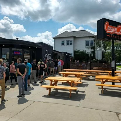 Busy barbecue restaurant with outdoor seating and a long line of customers