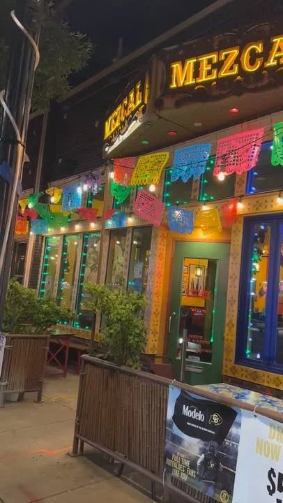 A vibrant restaurant exterior featuring colorful papel picado banners and festive lights, creating a lively atmosphere.