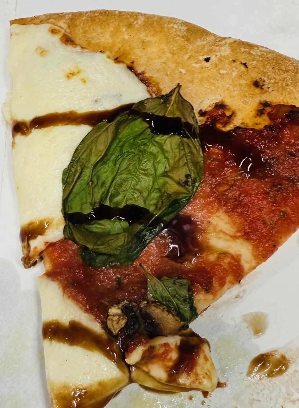 Slice of Margherita pizza with fresh basil and balsamic drizzle