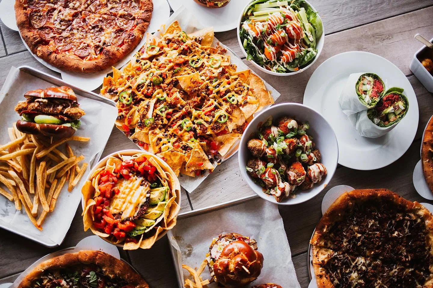 Assorted American comfort food including pizza, nachos, and burgers on a wooden table