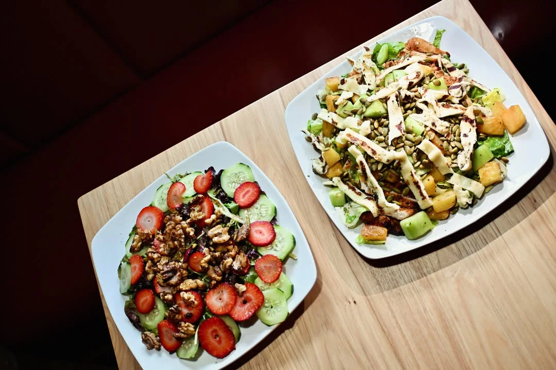 Two colorful salads displayed on white plates, featuring a mix of greens, fruits, and nuts.