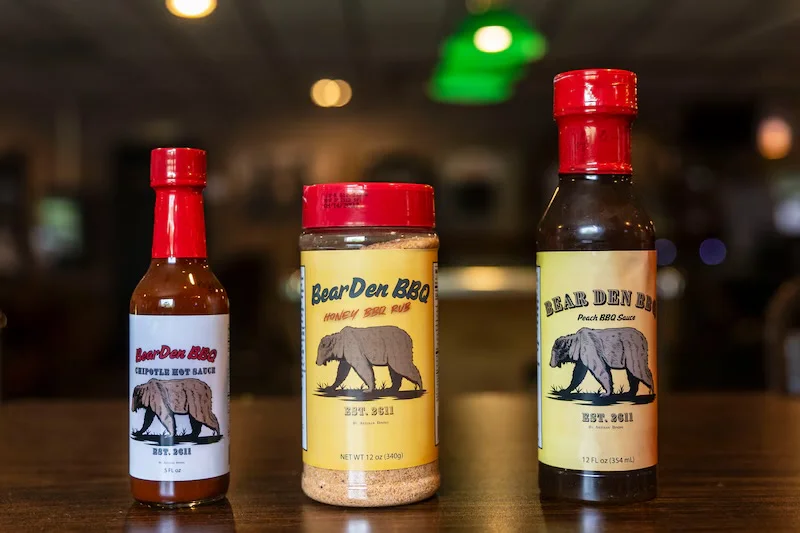 Bear Den BBQ sauces and rubs on a wooden table