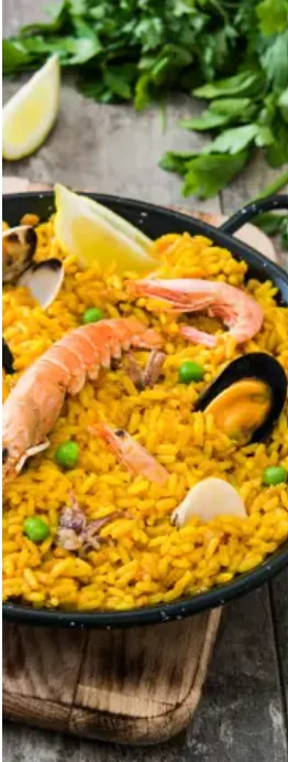 A large pan of yellow rice dish mixed with shrimp, mussels, and green peas, garnished with lemon wedges.