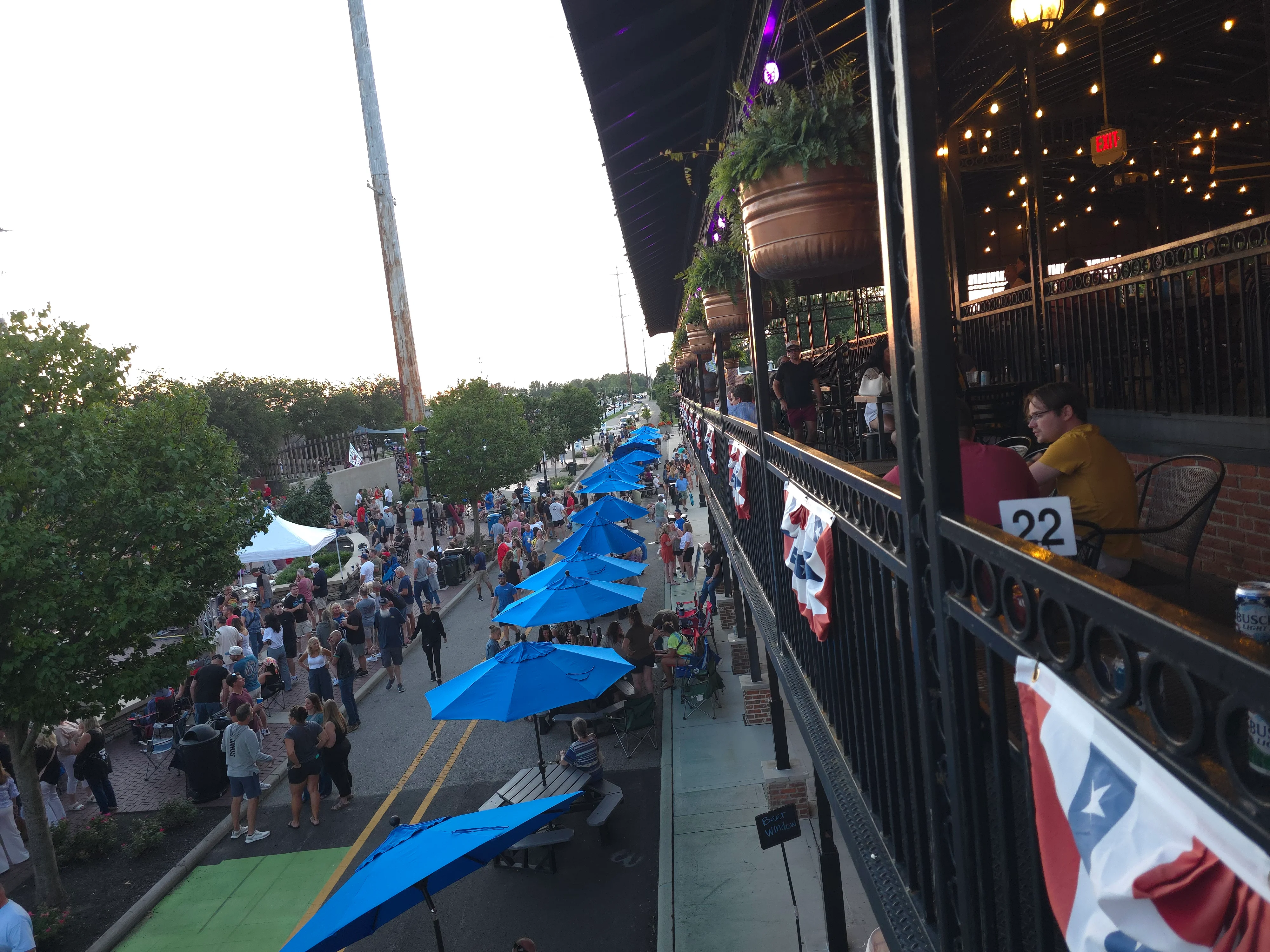 A bustling street filled with people enjoying an event, featuring umbrellas and decorative elements creating a celebratory mood.