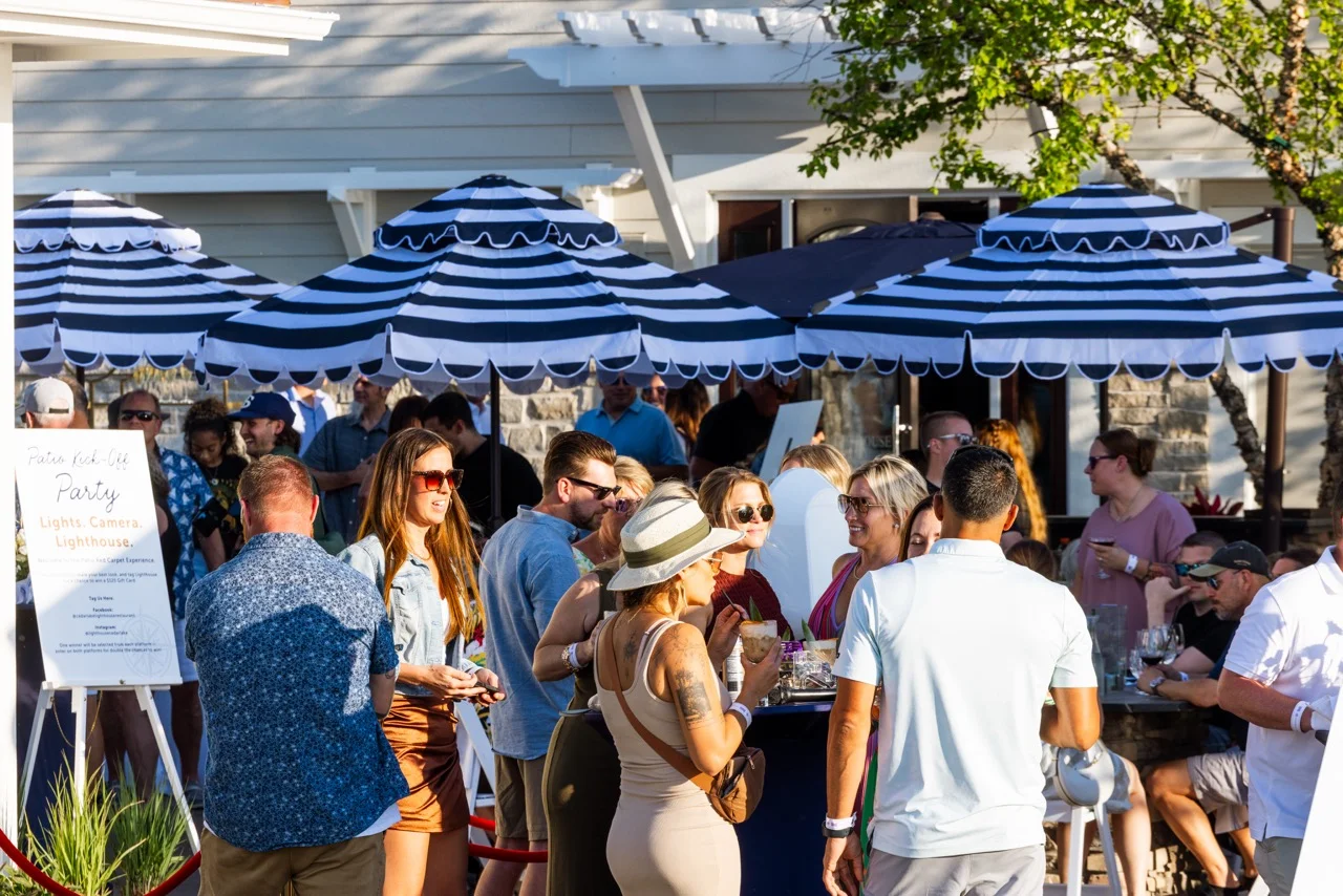 Outdoor party scene with guests enjoying drinks under striped umbrellas