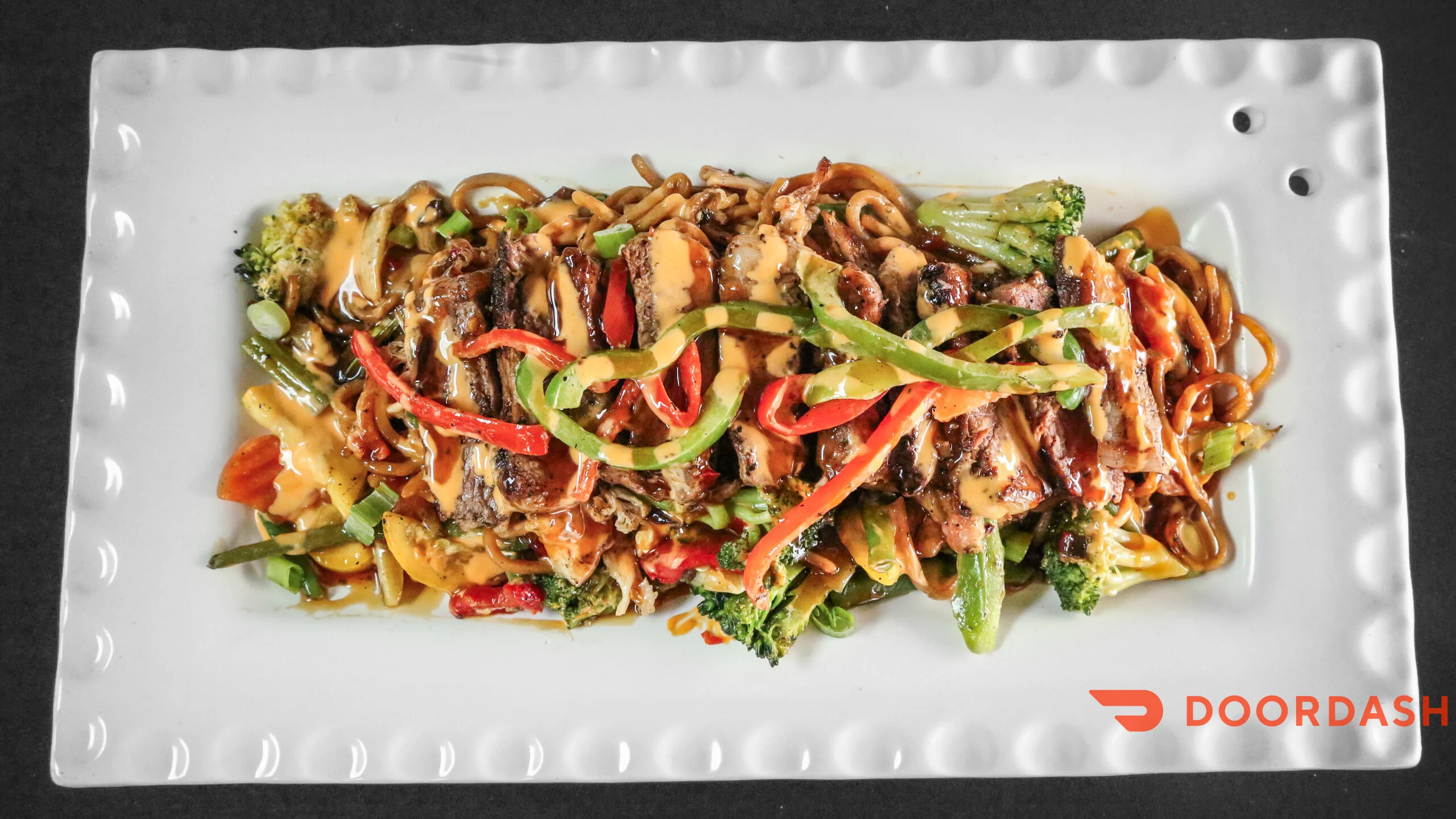 A generous serving of stir-fried noodles topped with sliced meats, colorful peppers, and a rich sauce.