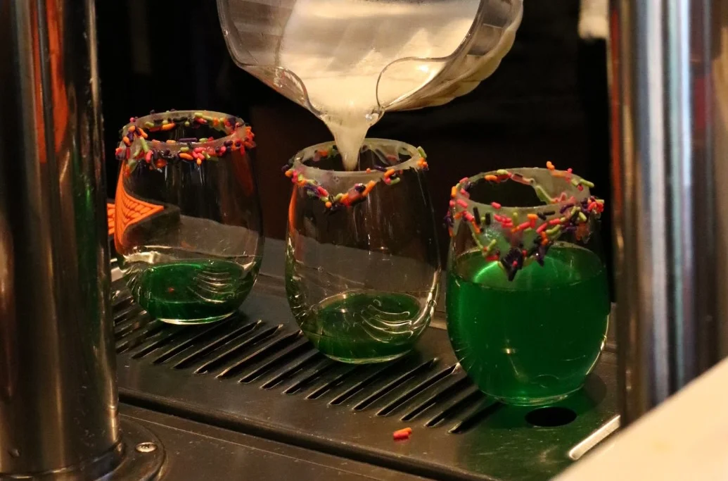 Bartender pouring colorful cocktails at a lively bar