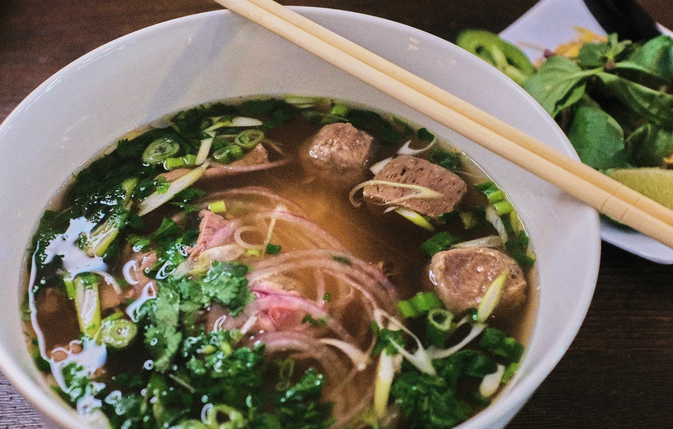 Bowl of Vietnamese pho with fresh herbs and meatballs