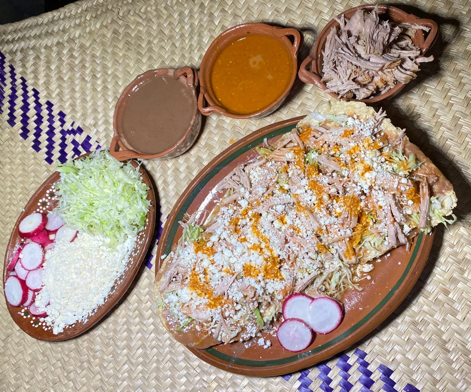 A large serving platter featuring a variety of shredded meat, topped with cabbage and cheese, along with sides of radishes and sauces.