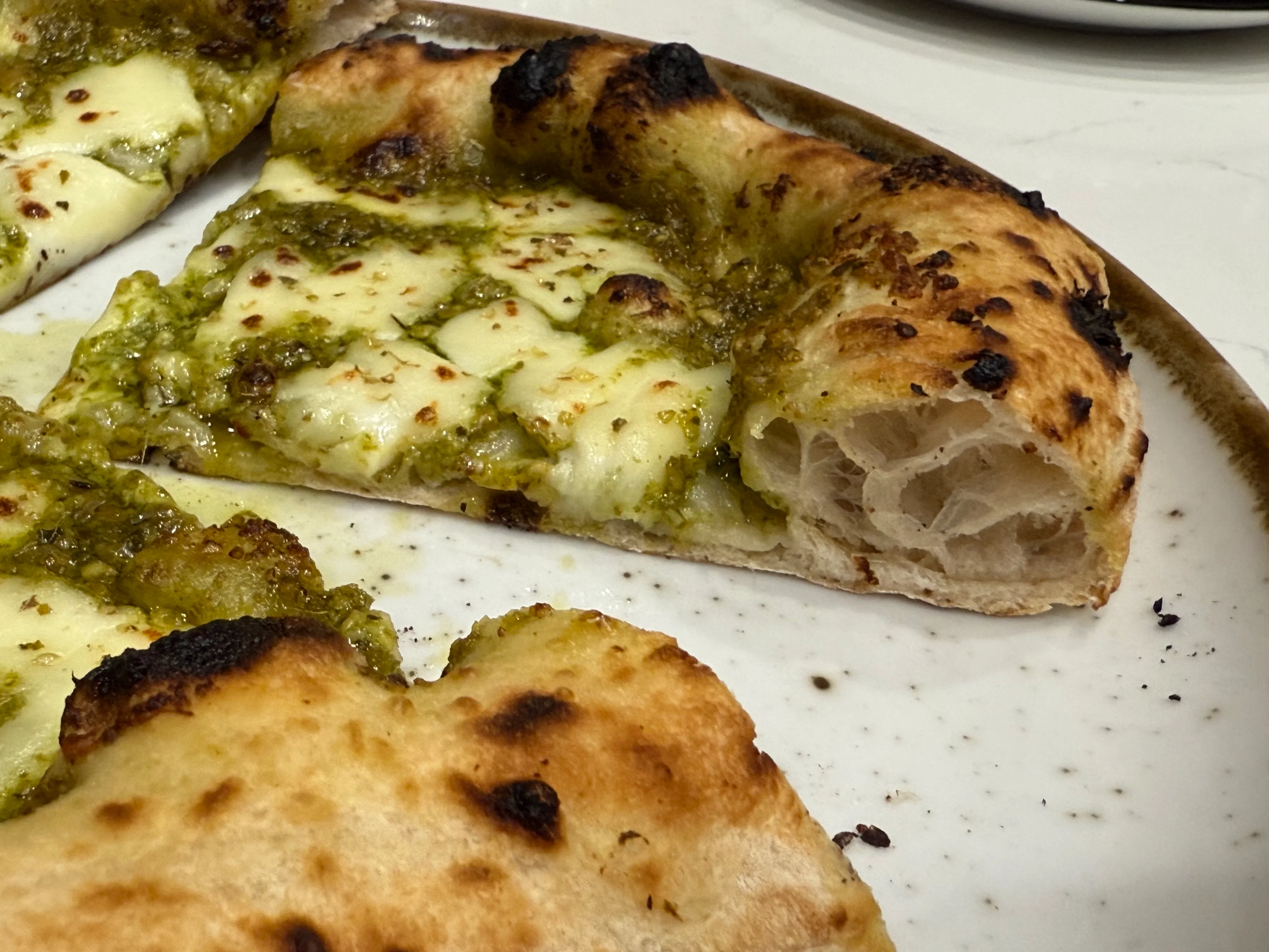 Pesto pizza with melted cheese and charred crust