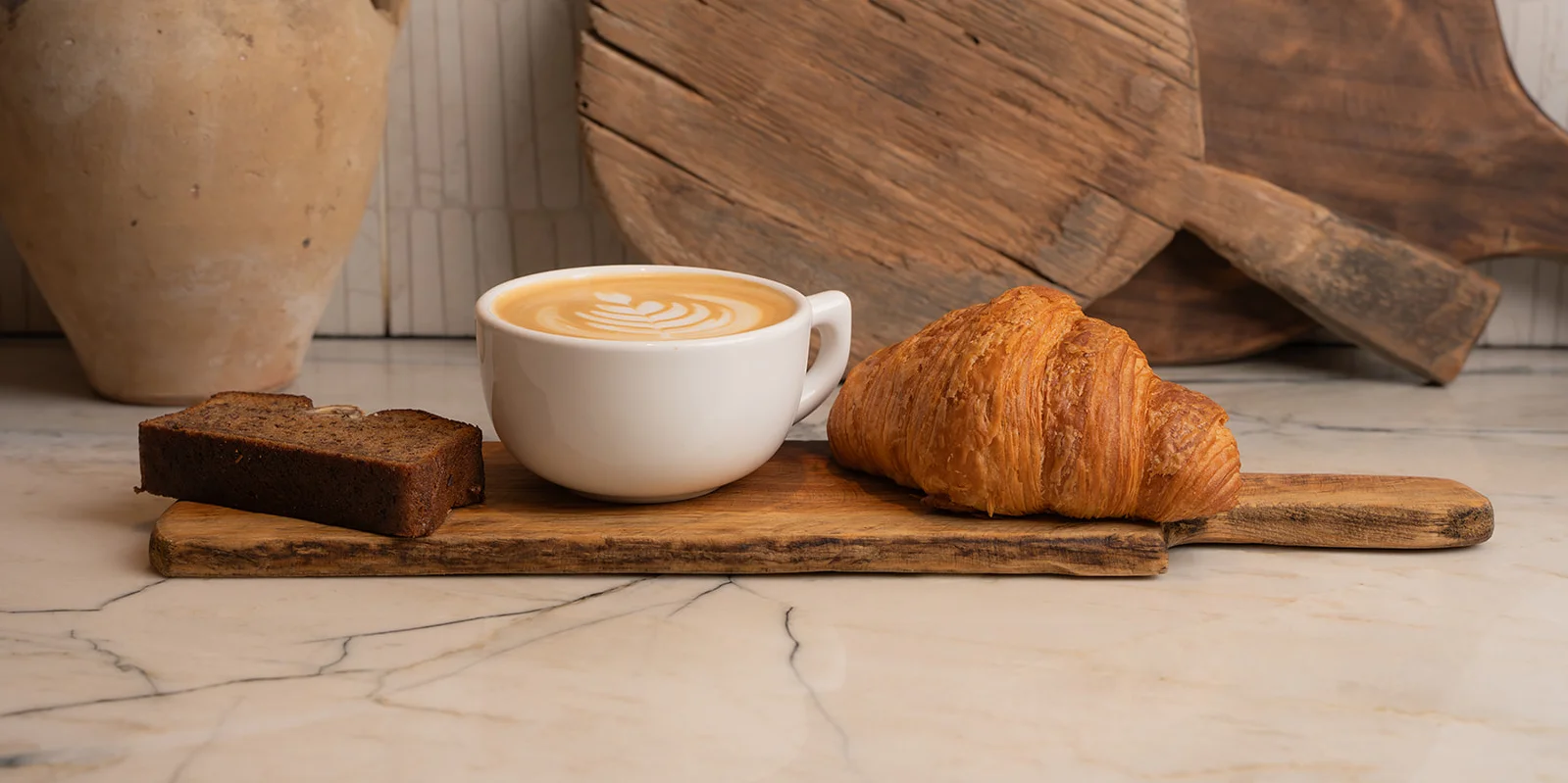Artisan coffee with croissant and cake on a wooden board