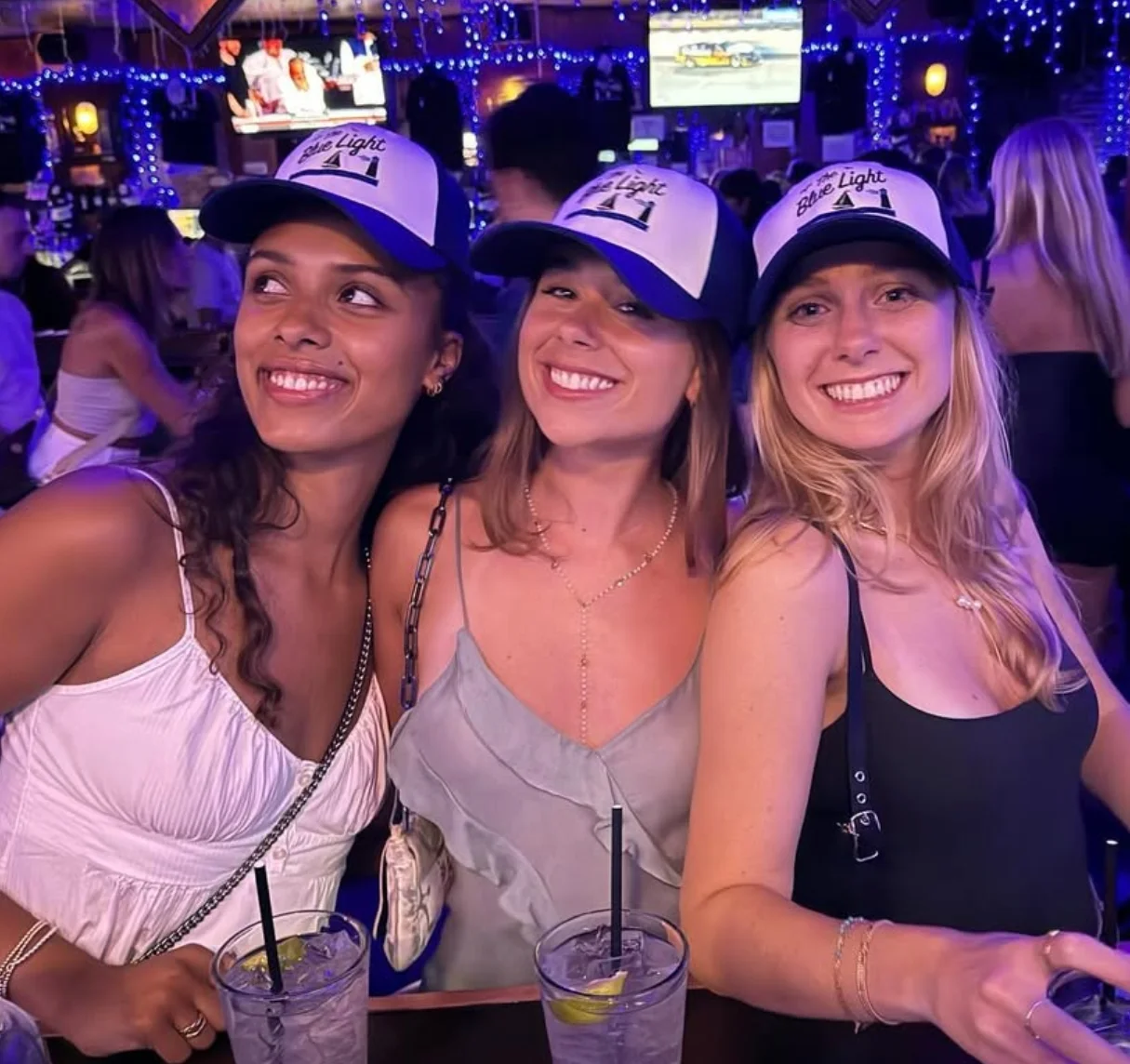 Three friends enjoying drinks at a lively bar with blue lighting