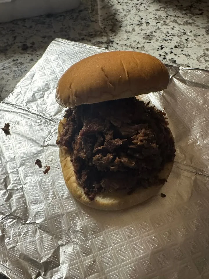 A sandwich filled with pulled meat, served on a soft bun on a silver foil wrapper.