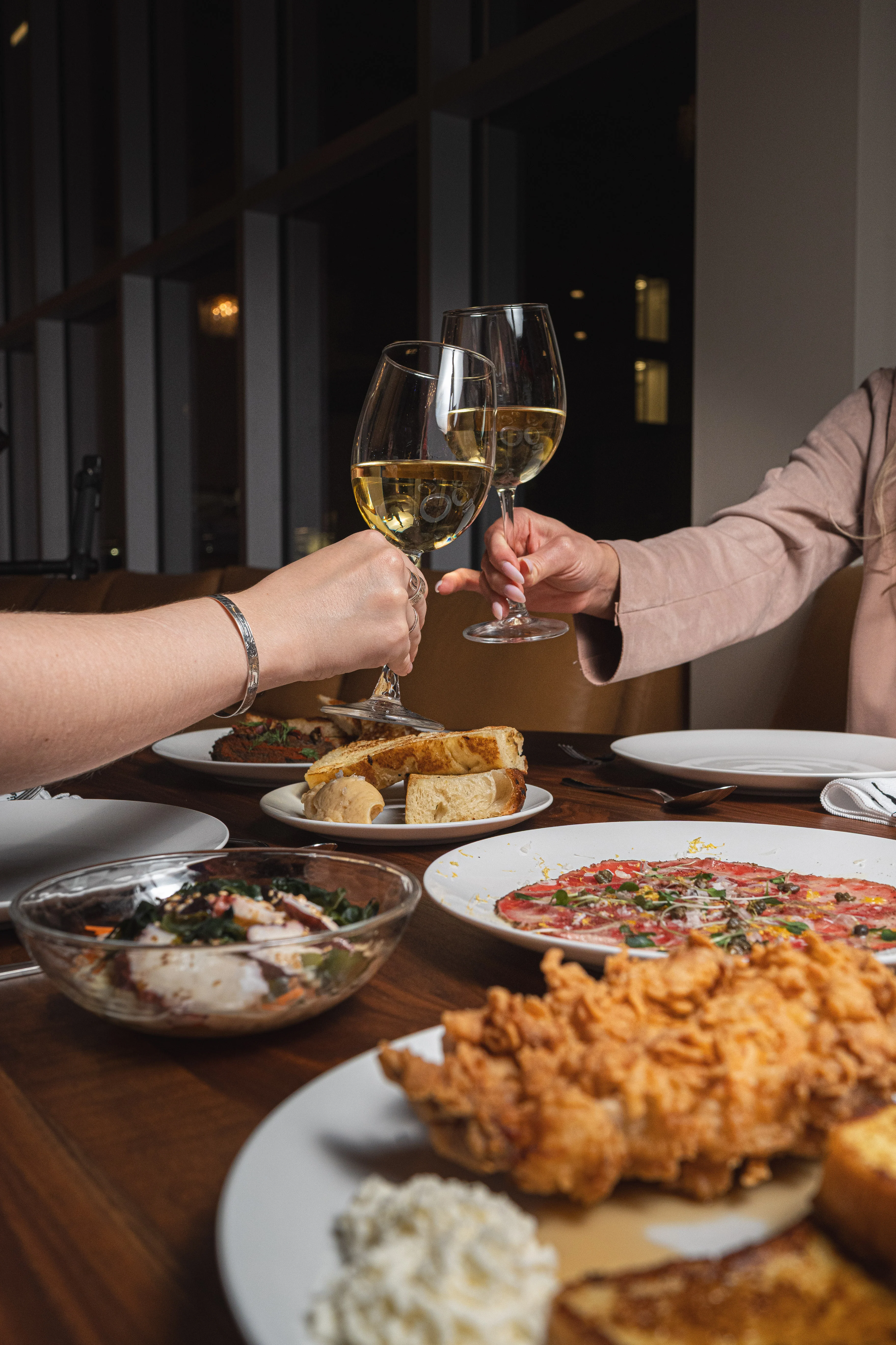Cheers with white wine glasses at a dining table with various dishes