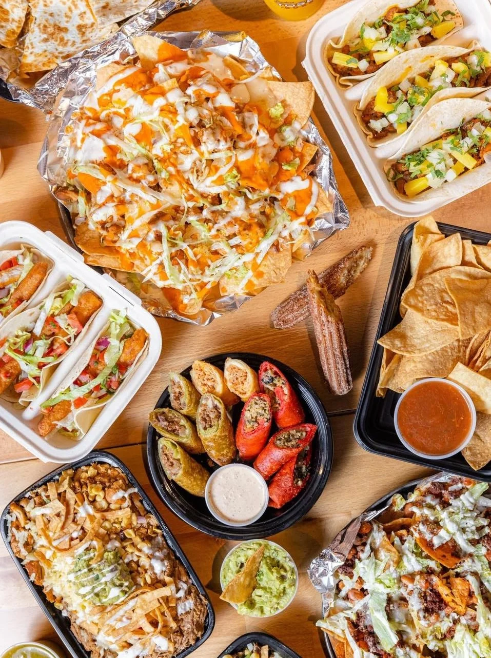 An assortment of various Mexican dishes including nachos, tacos, and burritos, presented on a wooden table.
